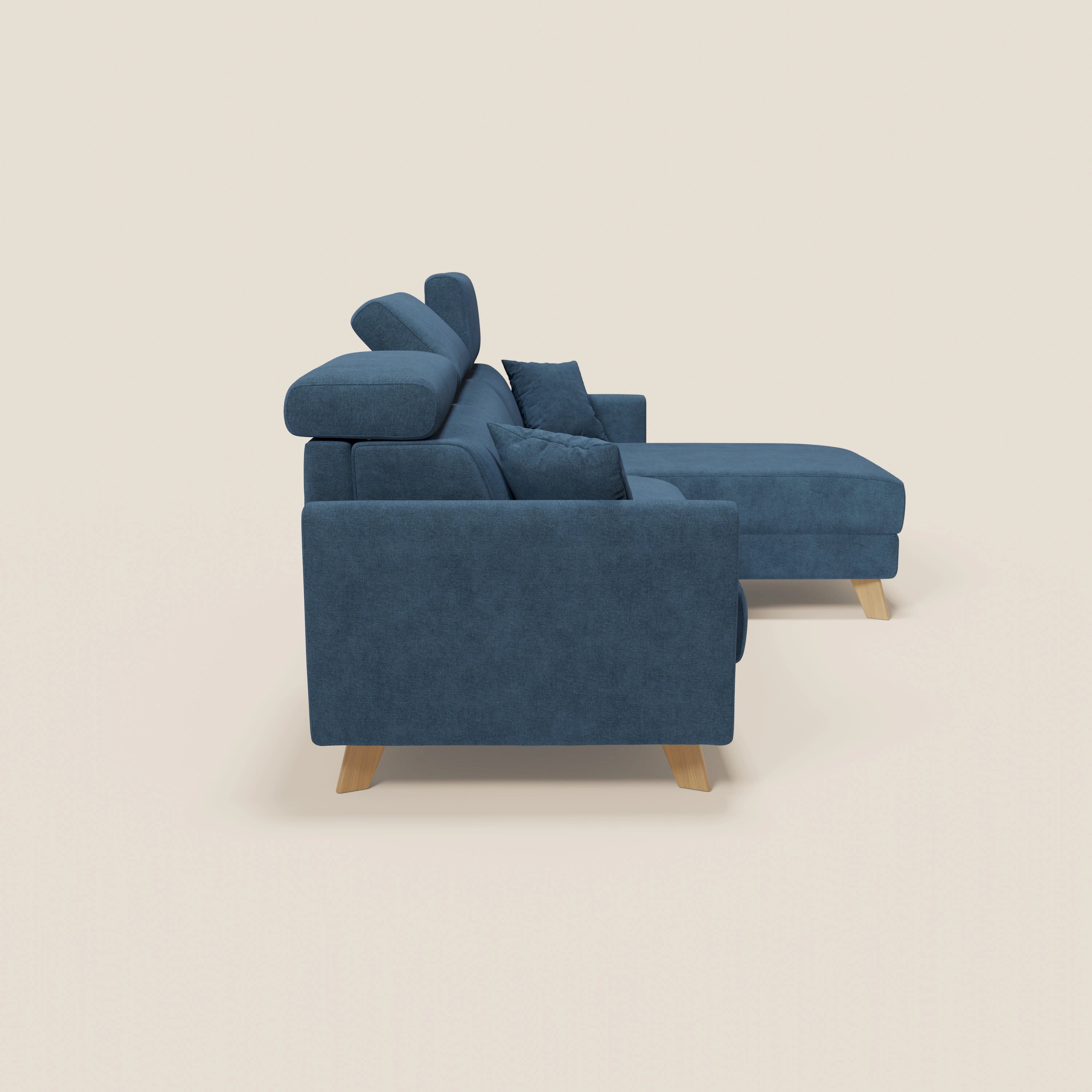 Il divano letto angolare sfoderabile Francy di Divani.Store, in tessuto antimacchia T17 blu, è caratterizzato da una chaise longue destra con contenitore, poggiatesta regolabili, gambe in legno chiaro e due cuscini coordinati su uno sfondo bianco sporco.
