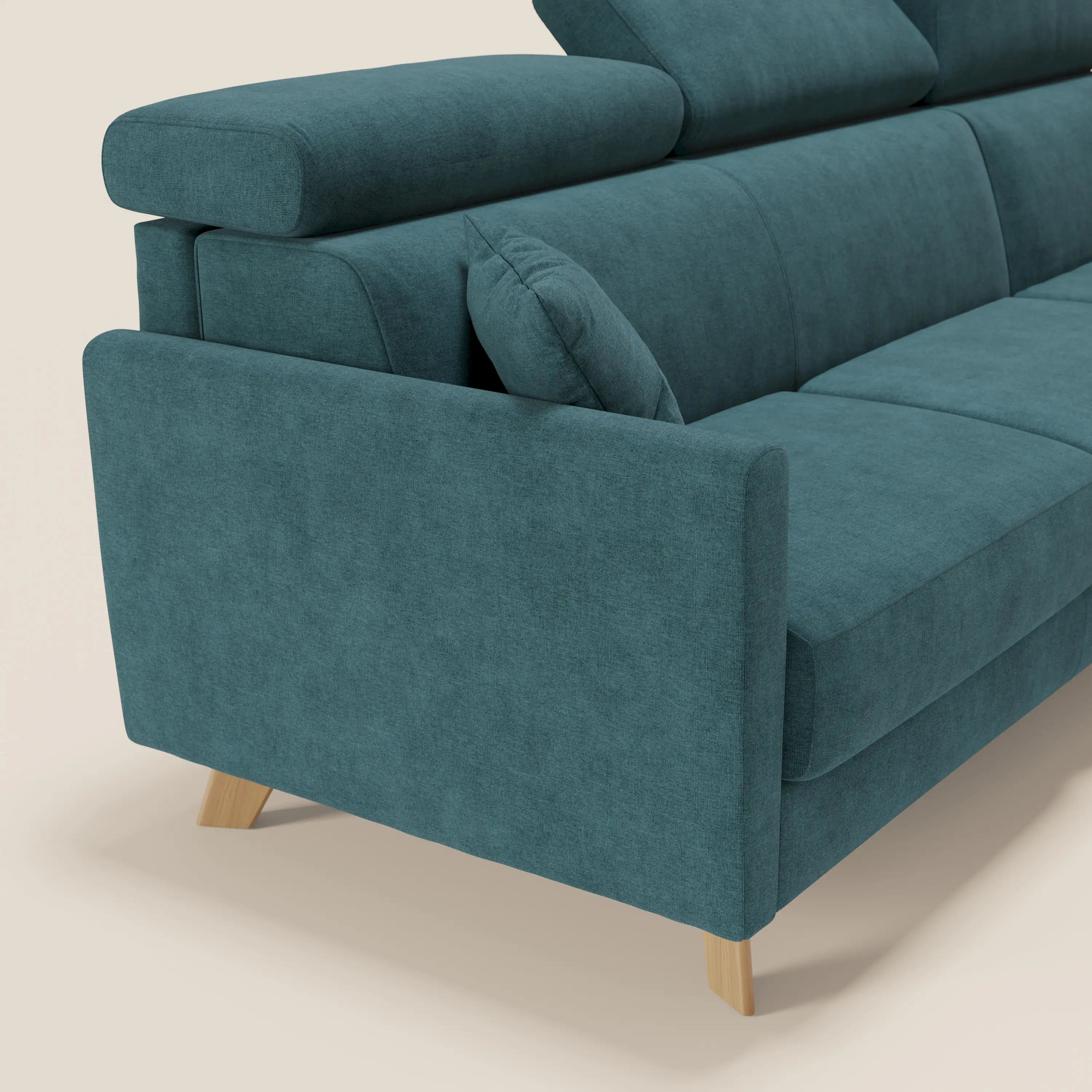 Il divano letto angolare sfoderabile Francy di Divani.Store, in tessuto smacchiabile T17 petrolio con penisola contenitore e poggiatesta reclinabili, è presentato affiancato da un cuscino coordinato su uno sfondo beige chiaro per un look nordico.