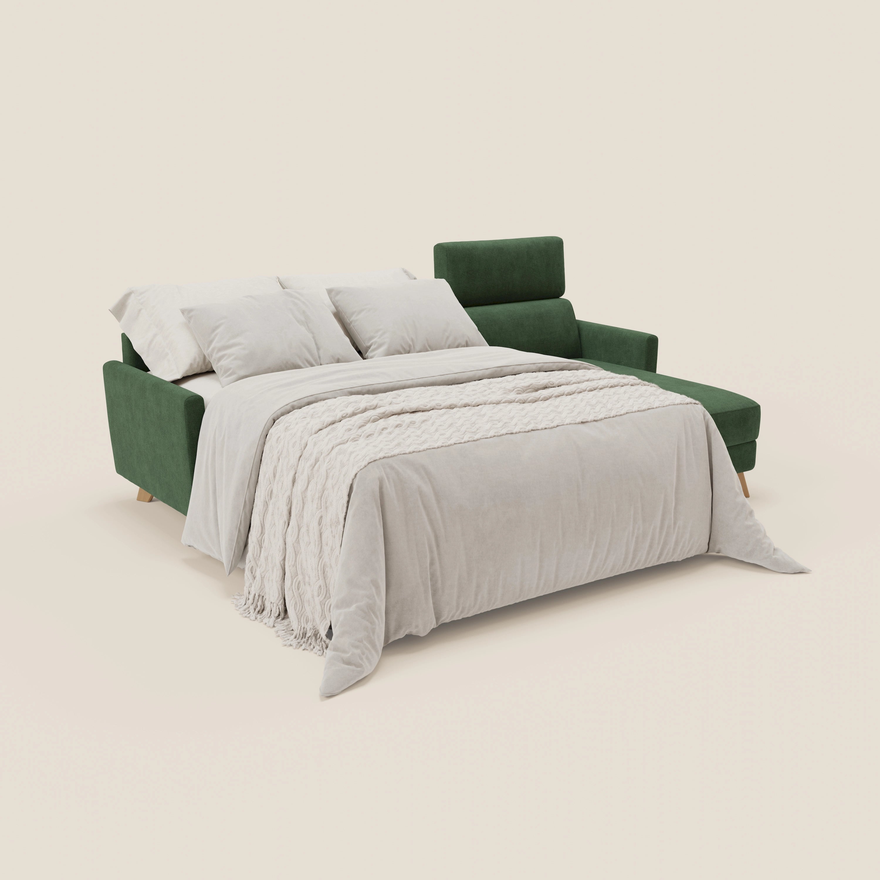 Il divano letto angolare sfoderabile Francy di Divani.Store in T17 verde si trasforma in un letto con lenzuola grigio chiaro, una coperta strutturata e tre cuscini, il tutto su uno sfondo bianco sporco per un look minimal e in stile nordico.