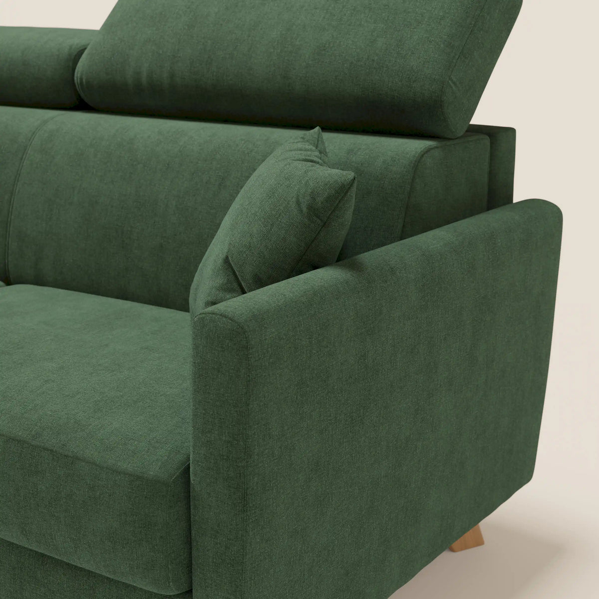 Un primo piano del divano letto matrimoniale Francy di Divani.Store, rivestito in tessuto T17 verde scuro, impermeabile e antimacchia, dotato di poggiatesta regolabili, bracciolo angolato, cuscino quadrato abbinato e poggiato su gambe in legno chiaro. Lo sfondo è semplice e neutro.