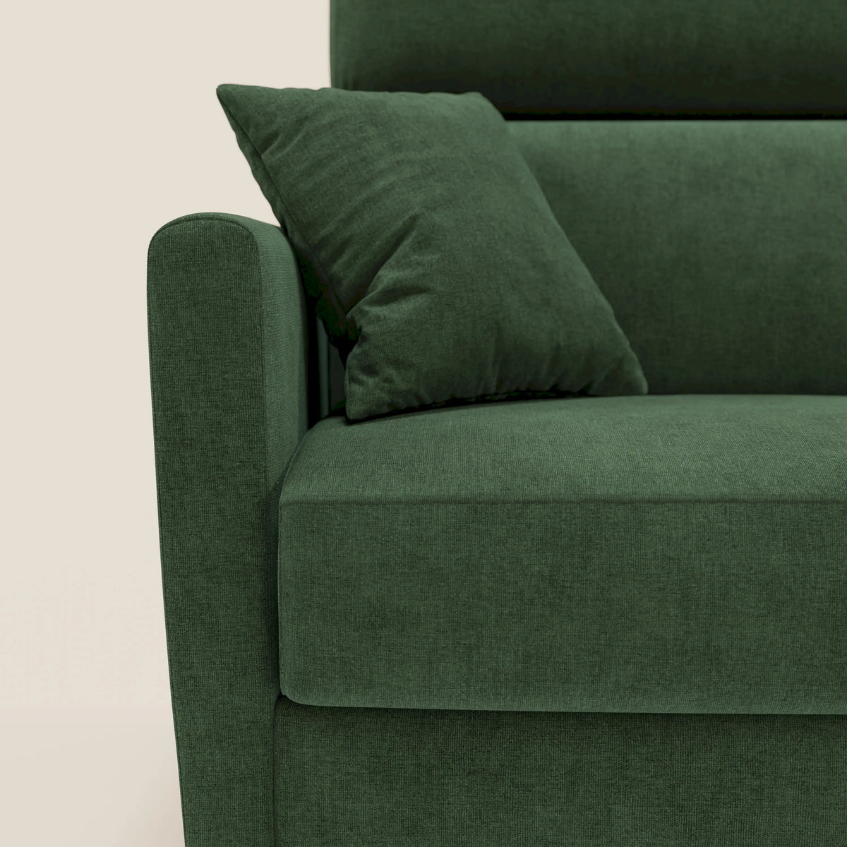 Un primo piano di un moderno divano in tessuto verde, come il divano letto matrimoniale Francy con poggiatesta regolabili da 180 cm (matr. 140x197) in tessuto impermeabile e smacchiabile T17 verde di Divani.Store, con un cuscino quadrato abbinato appoggiato sul bracciolo. Lo sfondo è di un colore beige chiaro a tinta unita. Nell’immagine sono visibili solo il lato sinistro e la seduta del divano letto Francy.