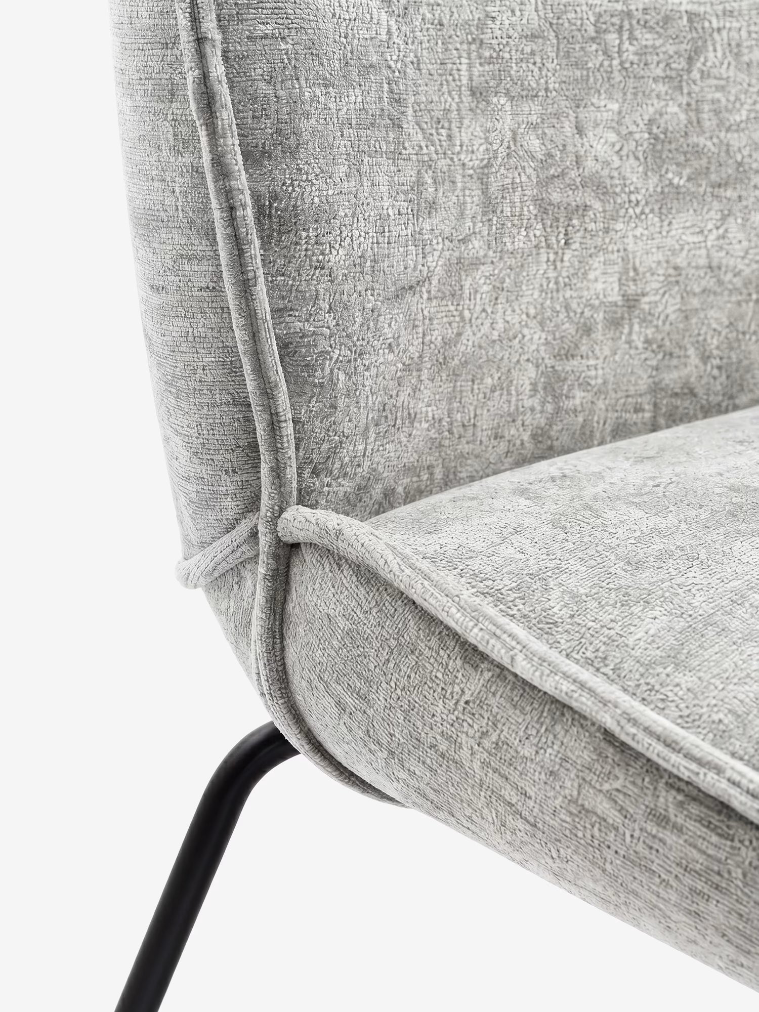 Primo piano di Iride, la sedia imbottita di Divani.Store in morbido tessuto materico grigio chiaro con cuciture a vista e struttura in metallo nero, dal design moderno con schienale e seduta curvi su sfondo bianco.