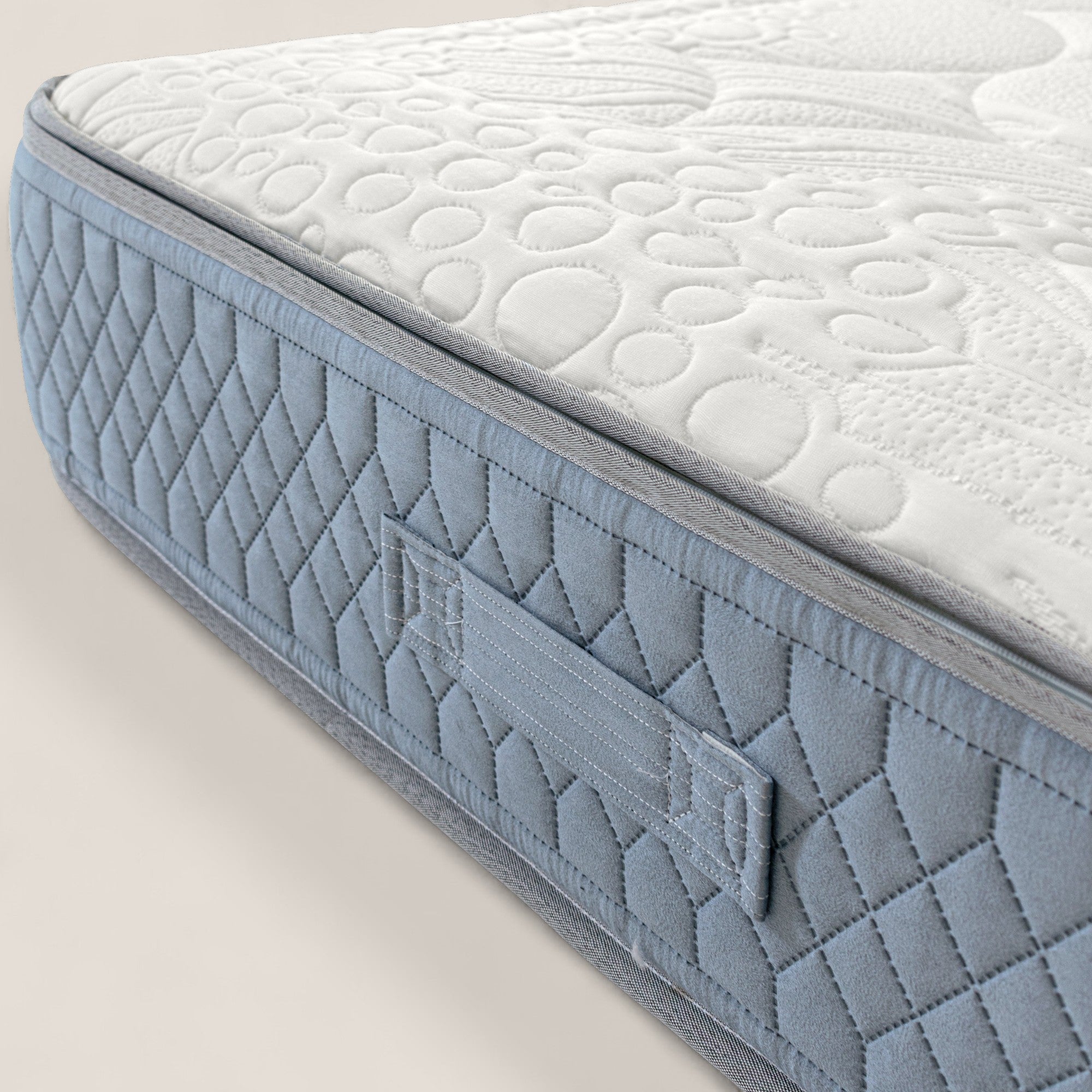 Primo piano di KYROS di Divani.Store: materasso di lusso con piano testurizzato bianco, lato trapuntato azzurro e maniglia impunturata. Dispone di un supporto posturale intelligente a 7 zone; tessuto morbido e cuciture resistenti per il massimo comfort.