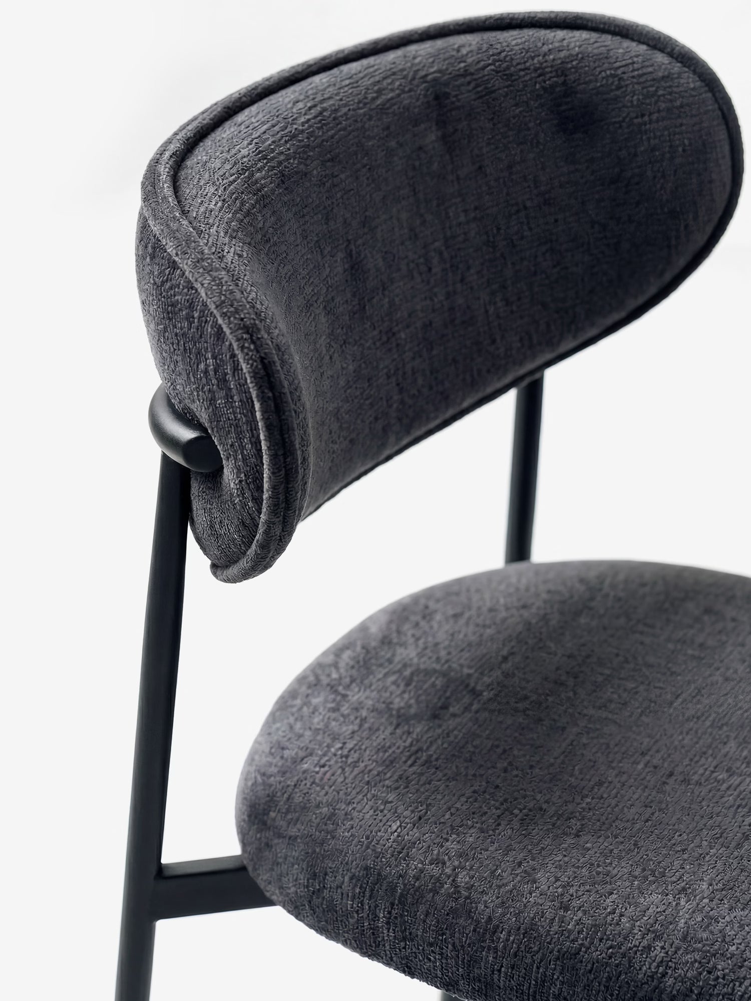Un primo piano della Luce Sedia, imbottita in morbido tessuto ciniglia di Divani.Store, che ne mette in risalto il lussuoso rivestimento grigio scuro e le forme arrotondate su un'elegante struttura in metallo nero, esaltandone il comfort e lo stile moderno su uno sfondo bianco.