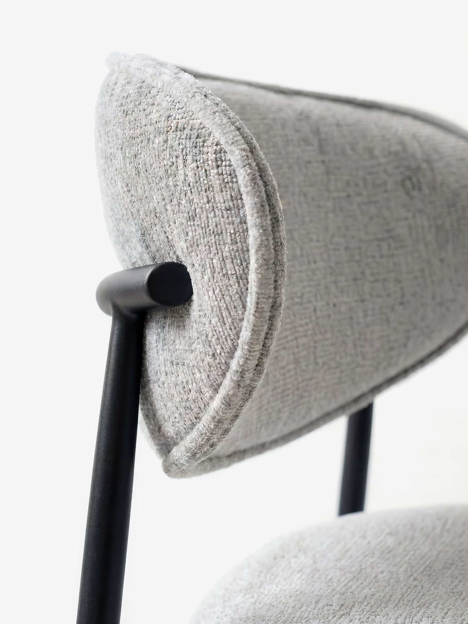 Primo piano della Luce Sedia, imbottita in morbido tessuto ciniglia chiaro di Divani.Store, che mette in risalto lo schienale arrotondato e la sottile struttura in metallo nero, per un design moderno ed elegante.