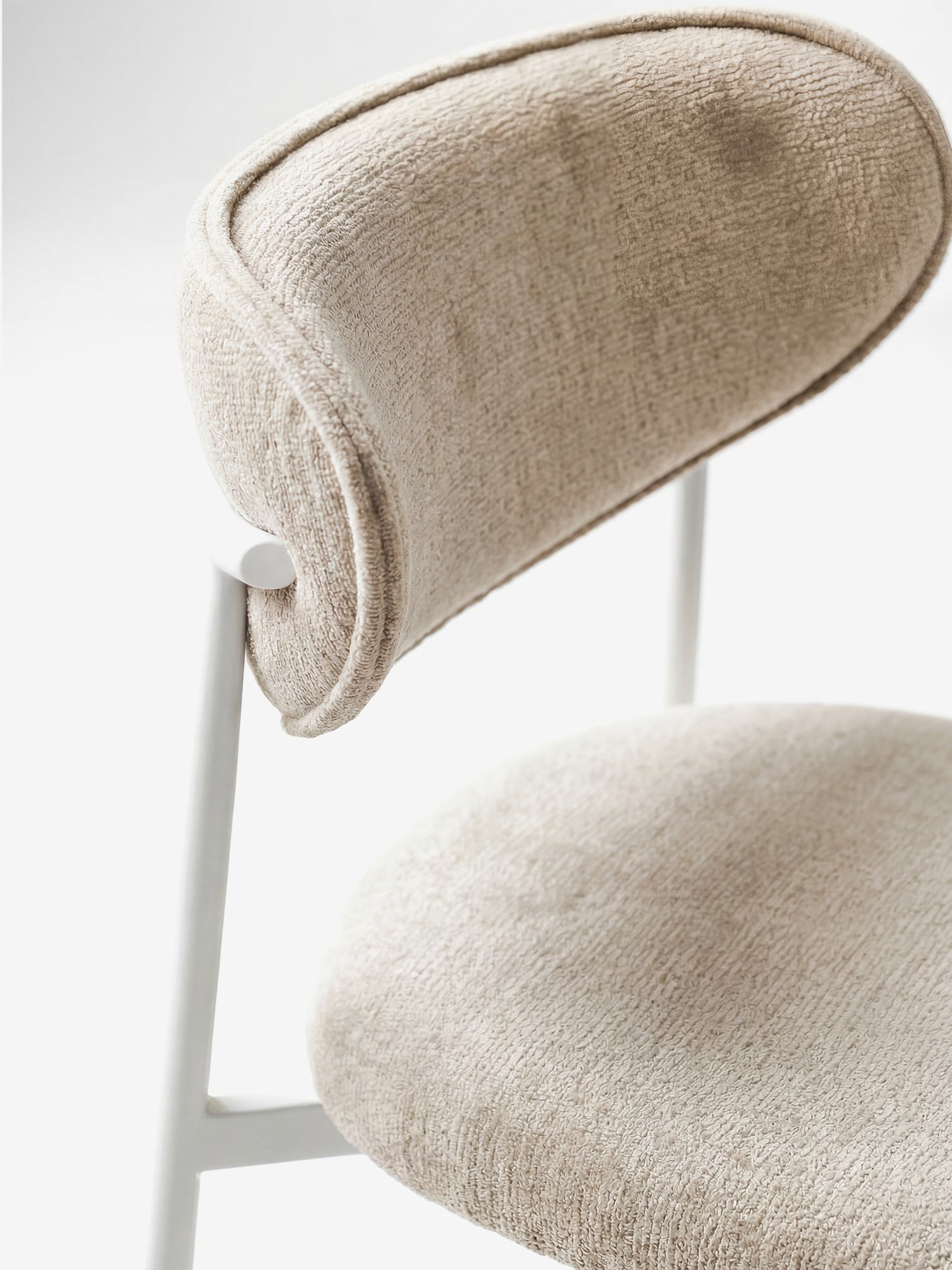 Un primo piano della “Luce Sedia imbottita con schienale curvo in tessuto con struttura in metallo bianco” di Divani.Store, caratterizzata da schienale e seduta imbottiti e curvi in tessuto beige chiaro, su uno sfondo bianco minimalista.