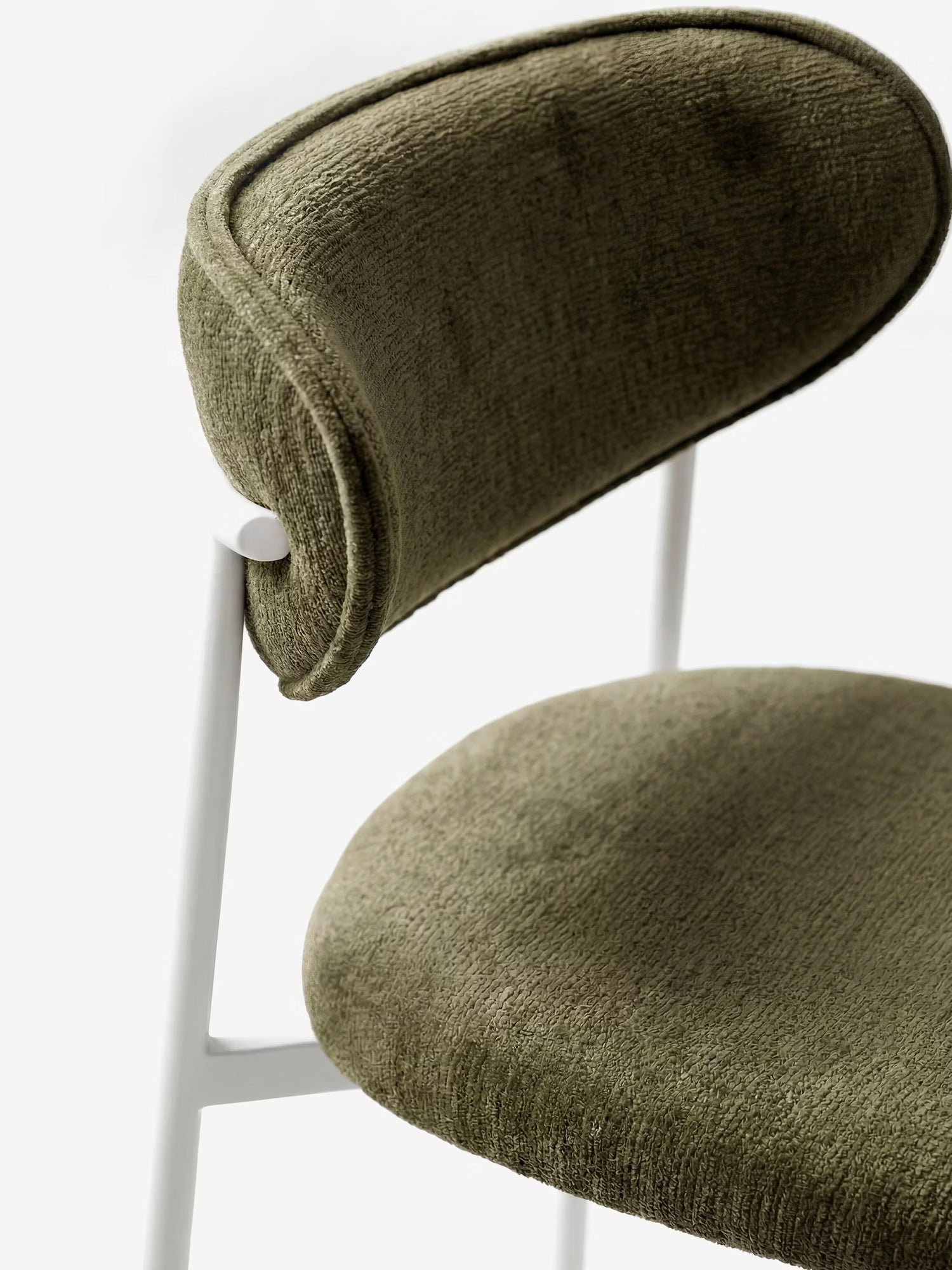 Primo piano della “Luce Sedia imbottita con schienale curvo in tessuto” di Divani.Store, caratterizzata da un tessuto testurizzato verde oliva e da un’elegante struttura in metallo bianco che ne esalta il design moderno su uno sfondo a tinta unita.