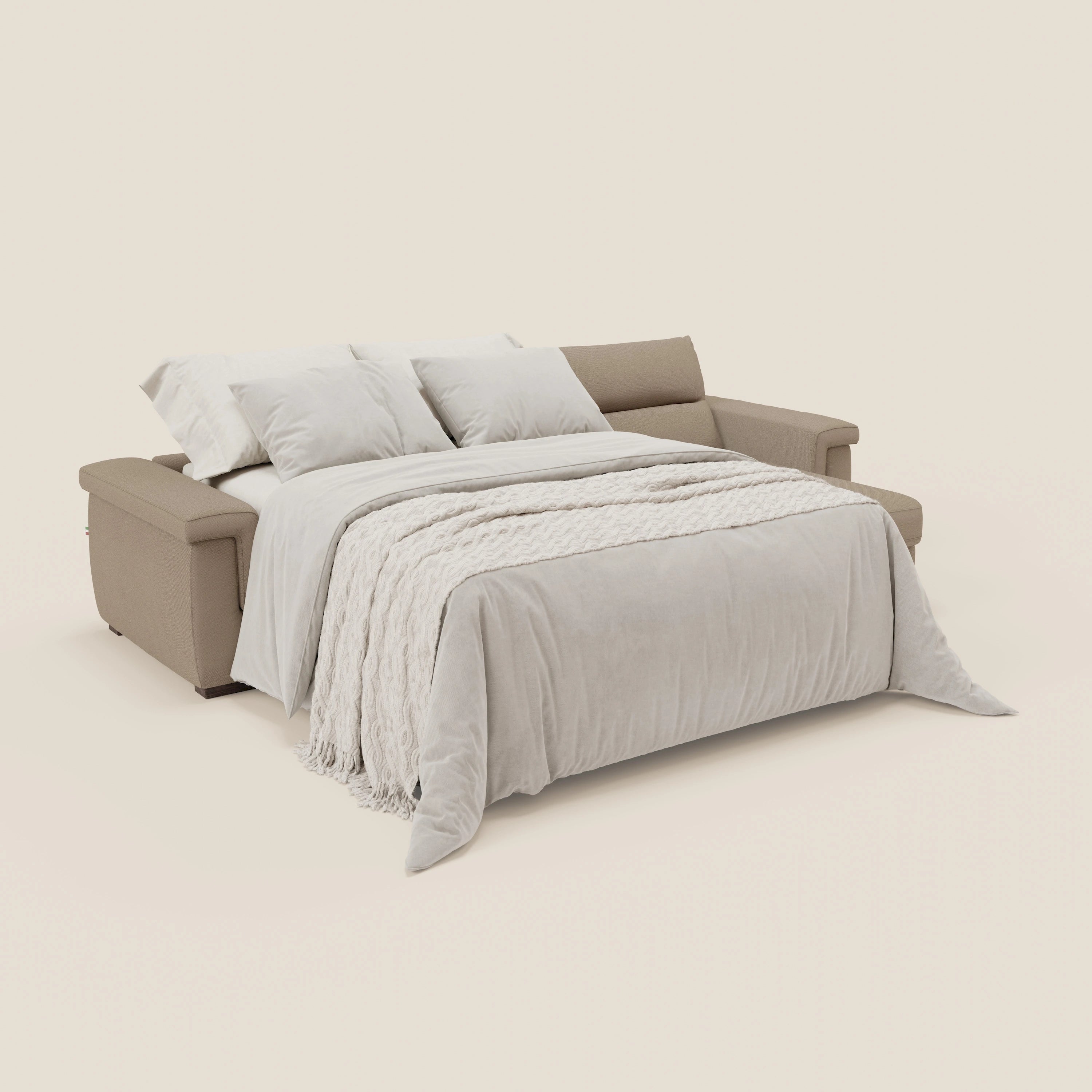 Il divano letto Magnolia angolare con Penisola Contenitore di Divani.Store in smacchiabile T05 beige si apre in un letto con piumone grigio chiaro, coperta bianca e tre cuscini bianchi su sfondo bianco sporco.