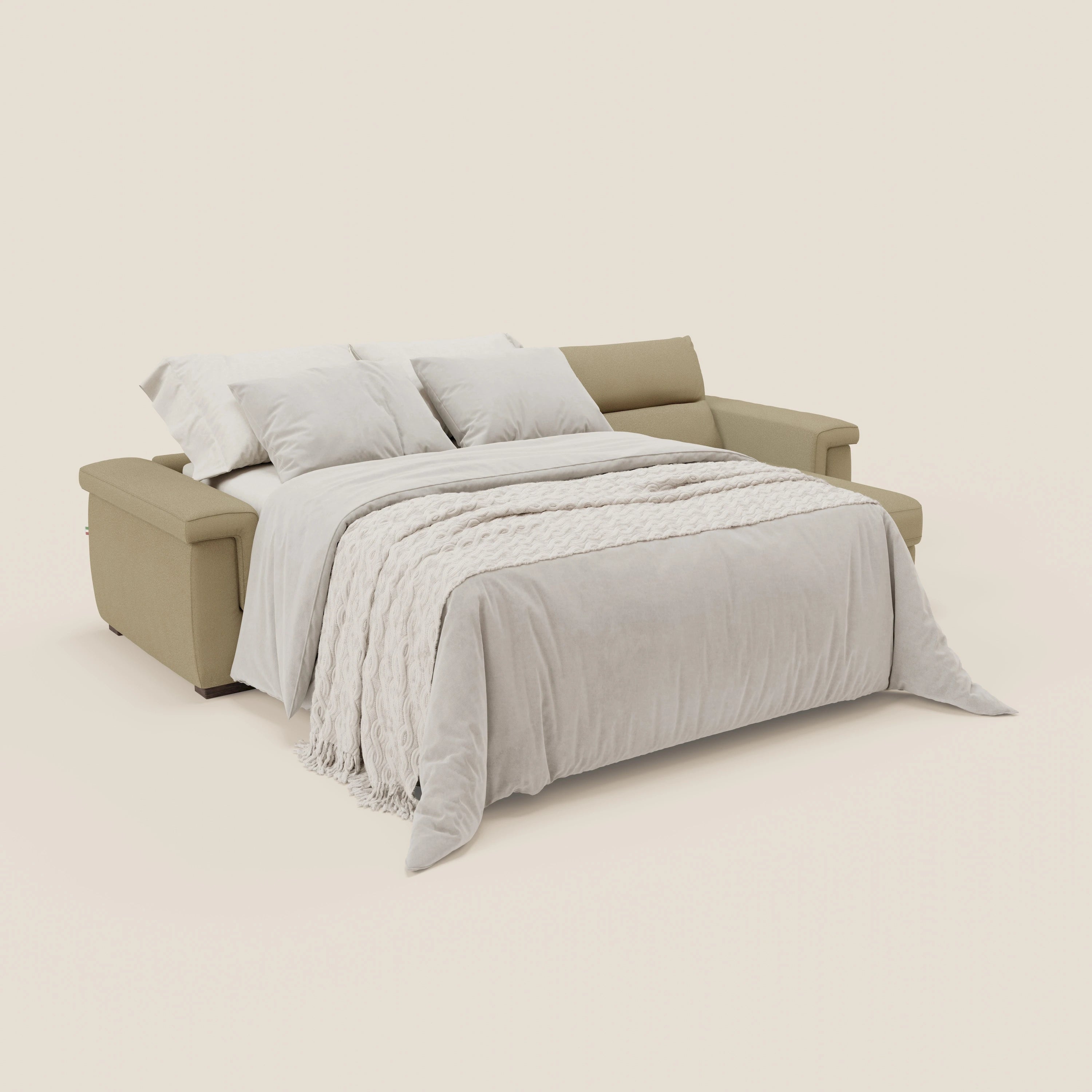 Il divano letto Magnolia angolare con Penisola Contenitore di Divani.Store in tessuto smacchiabile T05 cammello si trasforma in un letto con piumone grigio chiaro, parure crema e tre cuscini bianchi su sfondo bianco sporco.