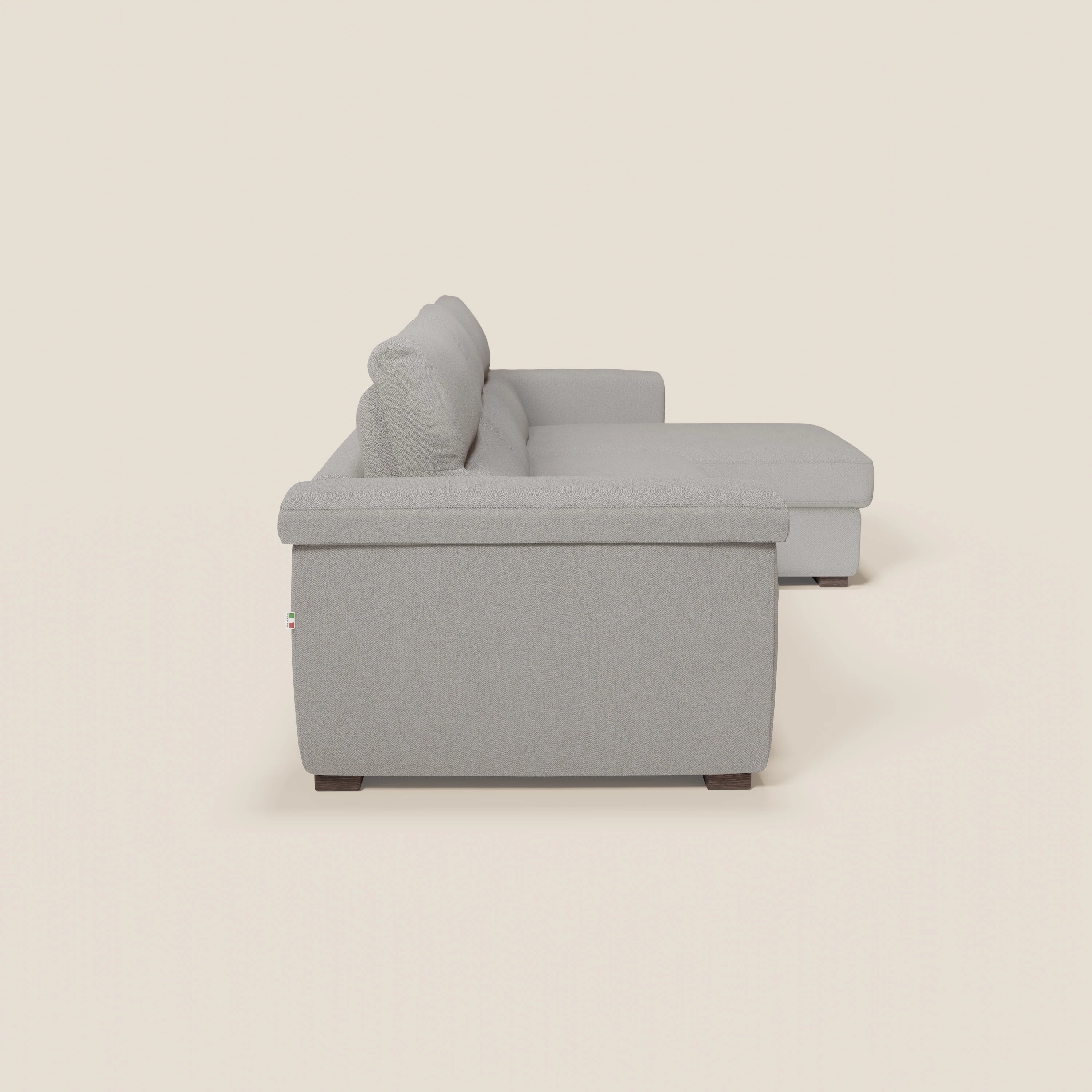 Il divano letto angolare Magnolia con penisola contenitore di Divani.Store, presentato in tessuto T05 grigio smacchiabile, è caratterizzato da cuscini spessi, una chaise rivolta verso destra, gambe corte in legno scuro e linee pulite e moderne su uno sfondo beige.