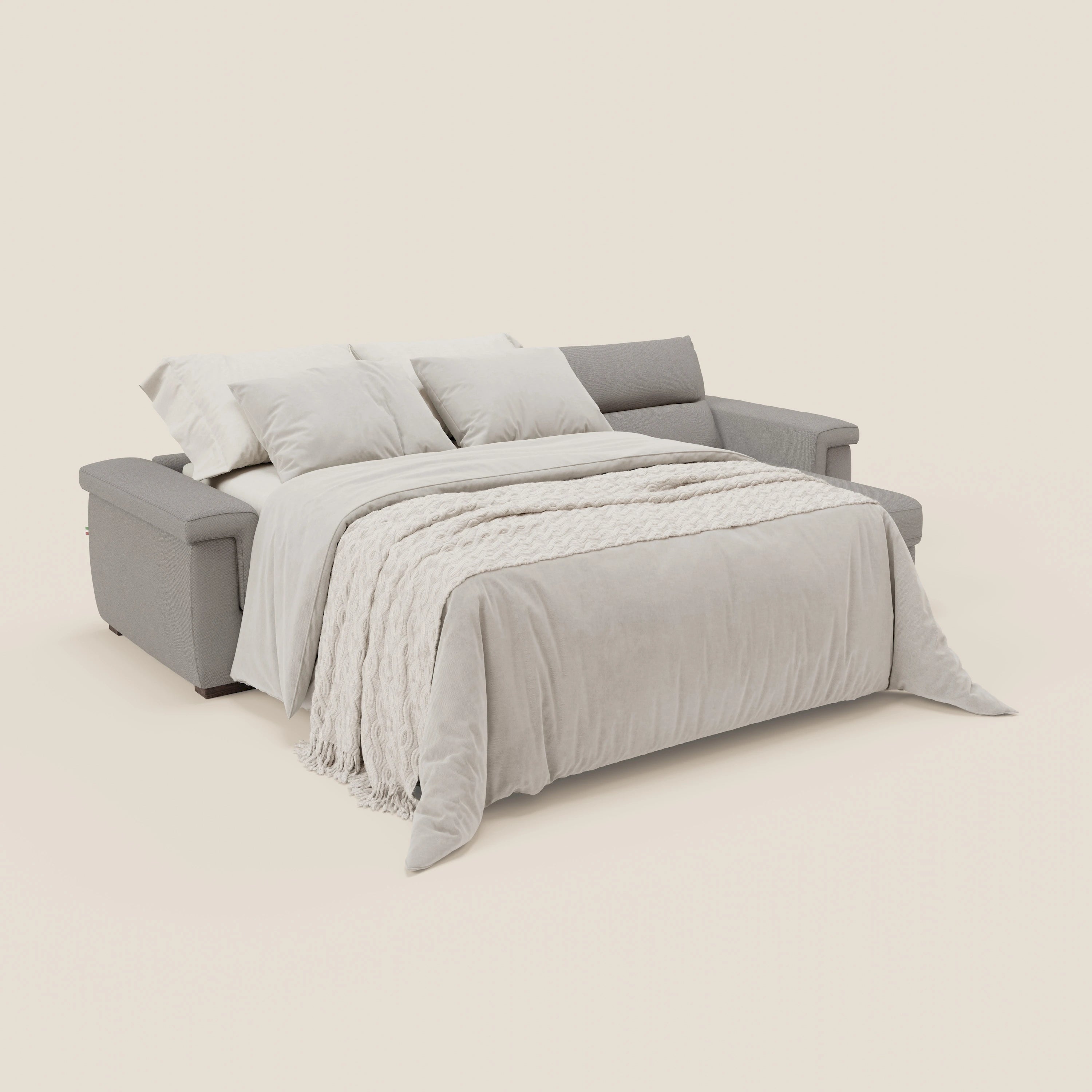 Il divano letto angolare Magnolia con penisola contenitore di Divani.Store, in tessuto smacchiabile T05 grigio con materasso H18 cm, è presentato accostato a una coperta beige chiaro e a tre cuscini su uno sfondo bianco sporco. Design contemporaneo con braccioli bassi.