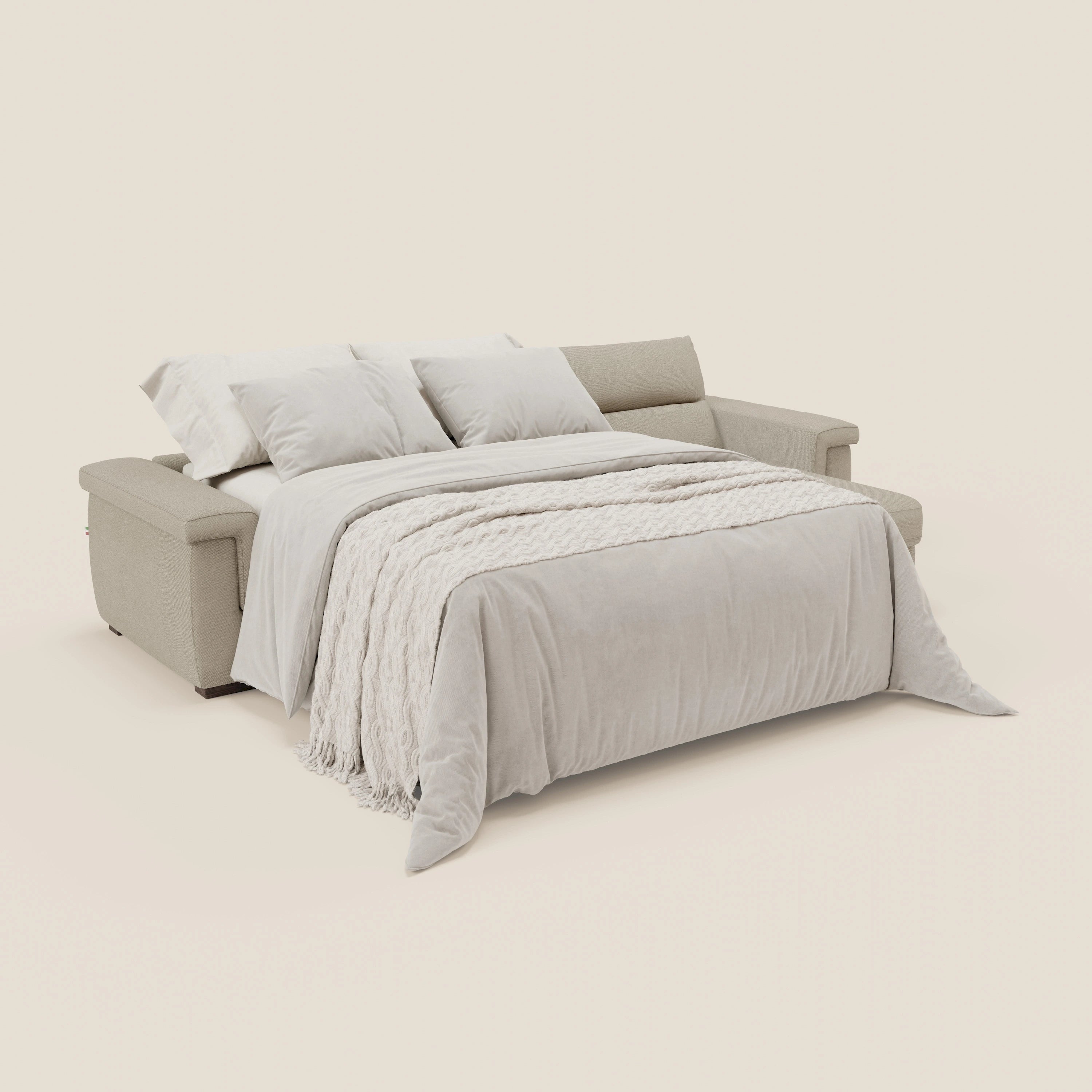 Il divano letto angolare Magnolia con Penisola Contenitore di Divani.Store si dispiega in un letto con biancheria in peluche, su uno sfondo bianco sporco che mette in risalto l'aspetto accogliente del tessuto antimacchia Panna T05 e del materasso H18 cm.