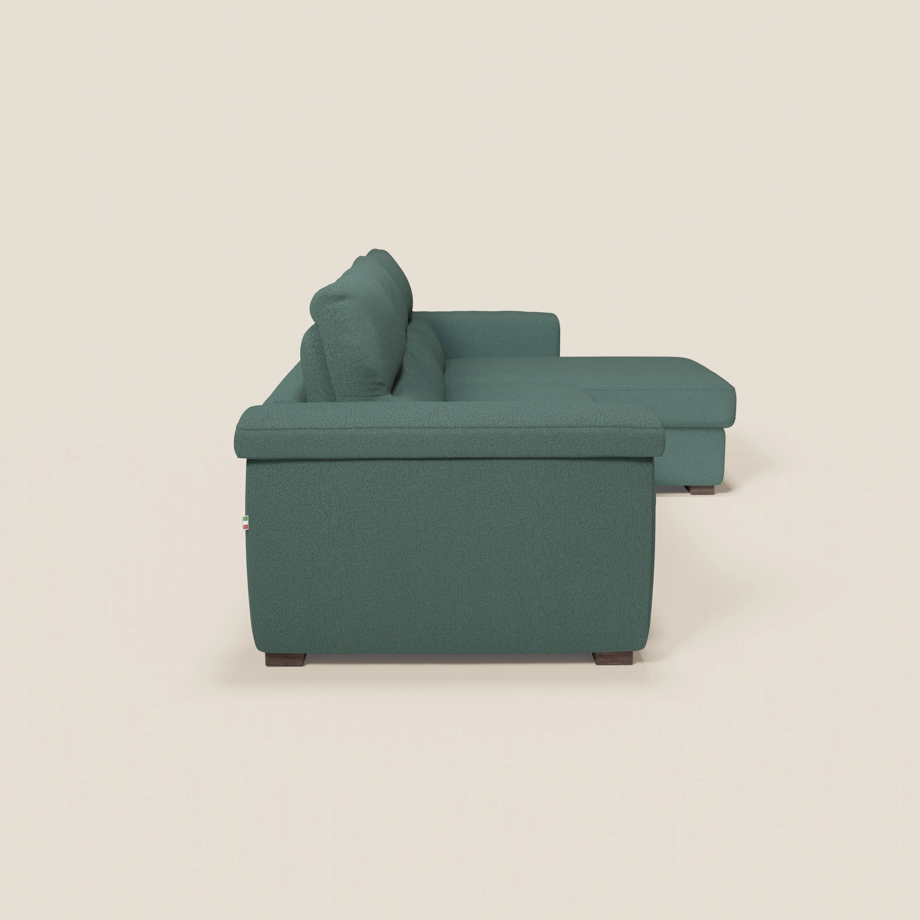 A Magnolia divano letto angolare con penisola contenitore di Divani.Store in tessuto smacchiabile T05 verde è mostrato lateralmente su sfondo chiaro, con cuscini spessi, braccioli, gambe scure e materasso H18 cm.