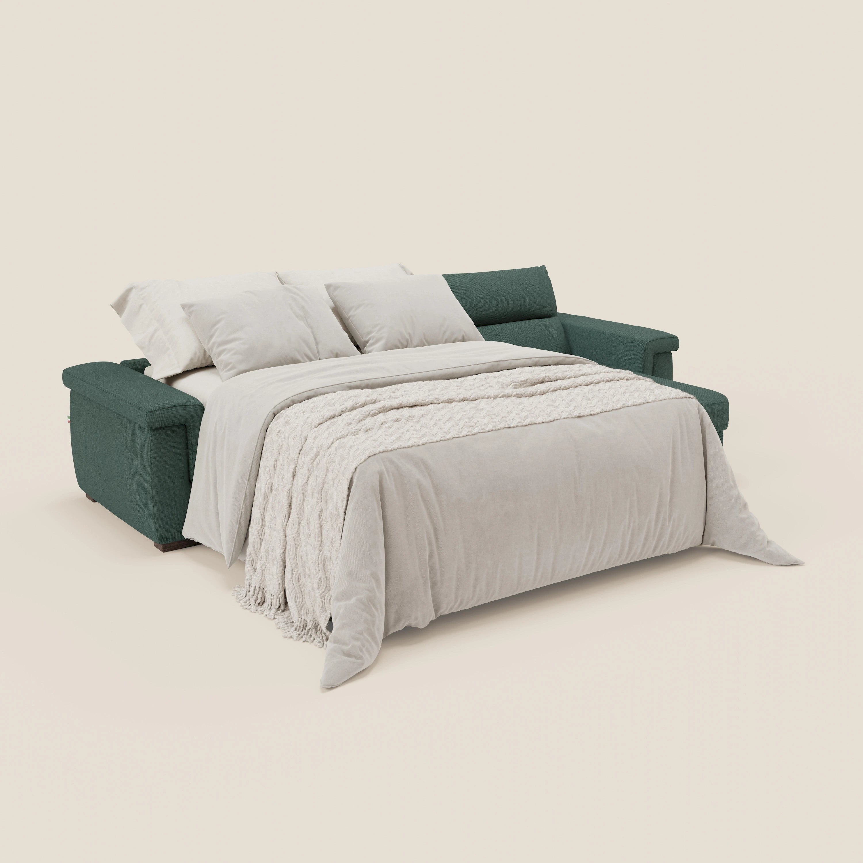 Un divano letto angolare Magnolia con Penisola Contenitore di Divani.Store in smacchiabile T05 verde viene allestito come letto con una trapunta color crema, due cuscini e una coperta color crema. Lo sfondo è un semplice beige chiaro.
