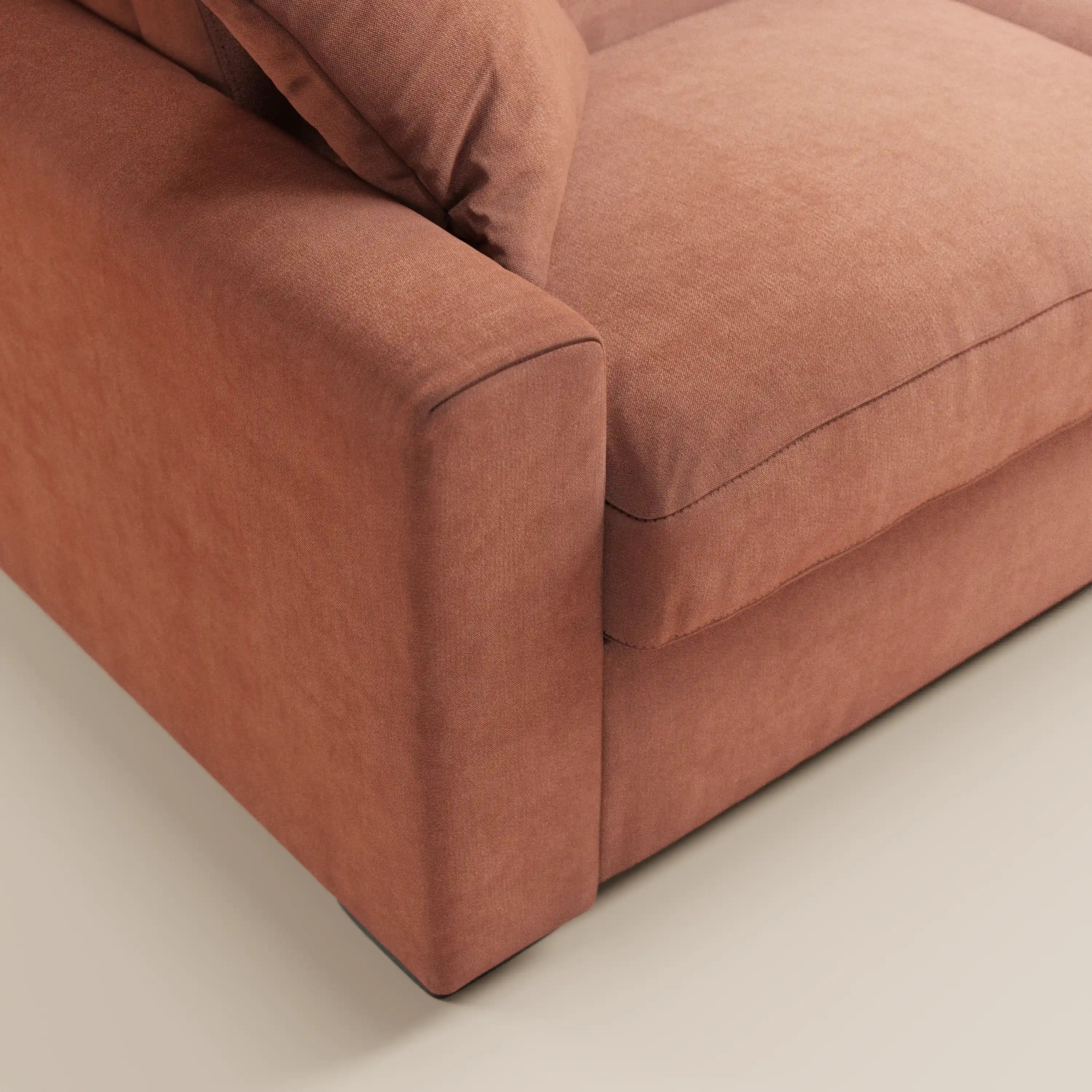 Primo piano del divano letto a 3 posti Maximus di Divani.Store, con rivestimento in tessuto Oeko-Tex resistente alle macchie color ruggine, braccioli spessi, morbidi cuscini di seduta e schienale, su un pavimento chiaro. Tra le caratteristiche figurano un materasso alto 20 cm e poggiatesta reclinabili.
