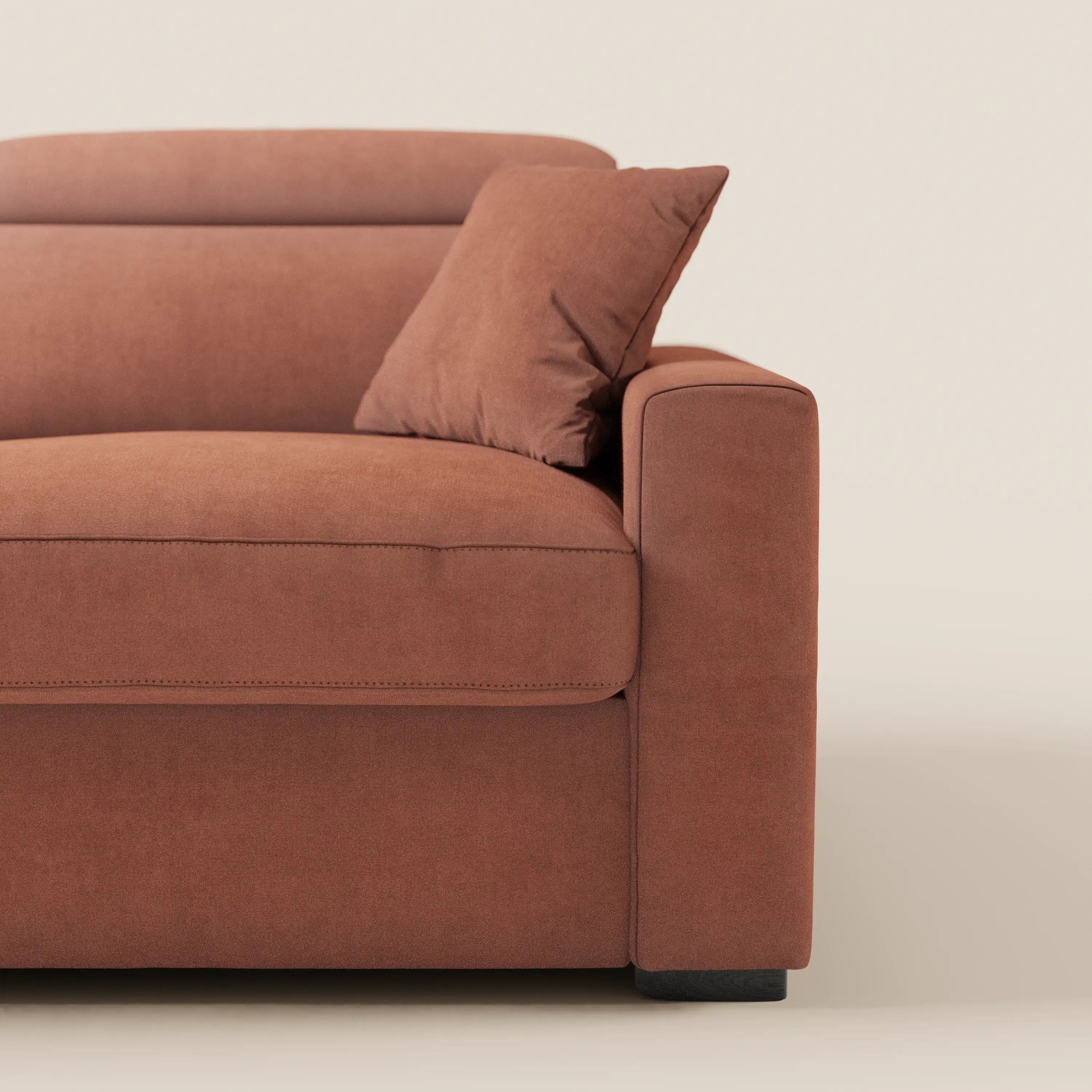 Primo piano del lato destro del divano letto Maximus a 3 posti con materasso ALTO 20 cm di Divani.Store, realizzato in tessuto Oeko-Tex color ruggine e resistente alle macchie, con poggiatesta reclinabili, cuscino coordinato, linee pulite e gambe corte nere su uno sfondo chiaro.