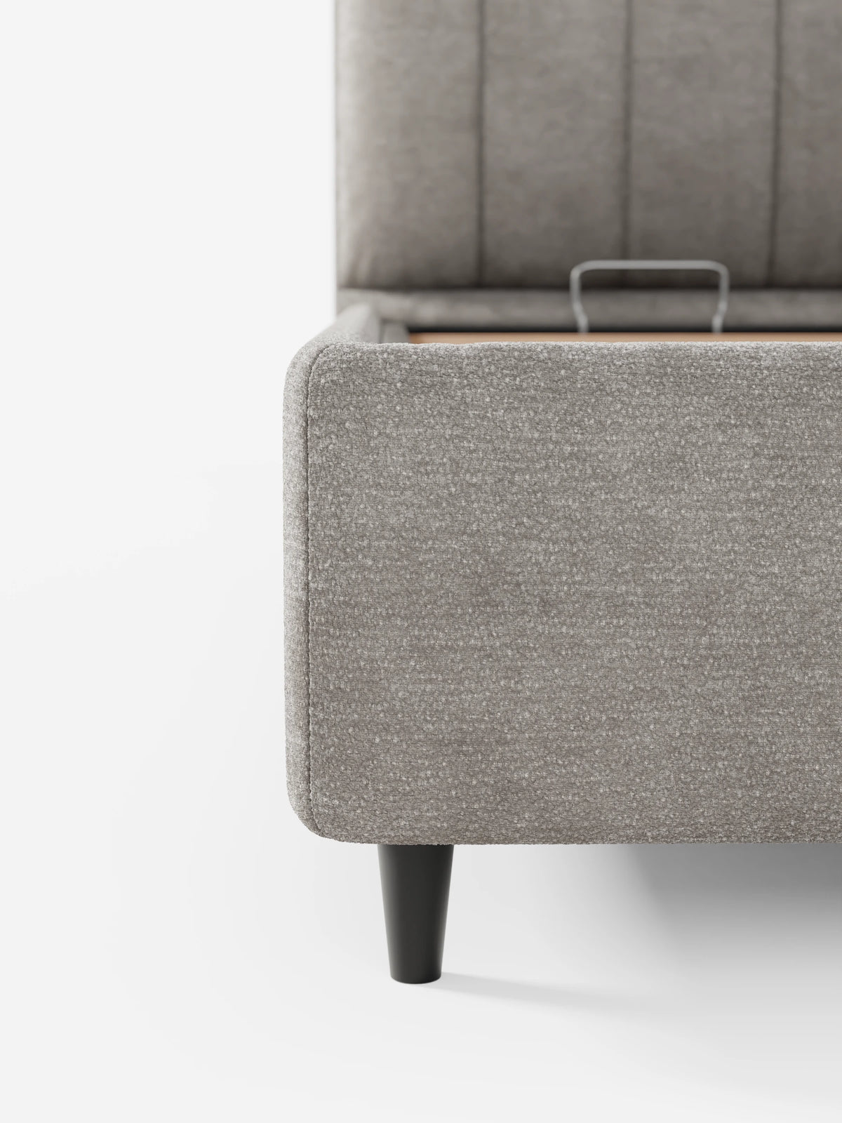Un primo piano di un divano letto ONYX color taupe con vano contenitore e testiera a pannelli verticali in tessuto certificato Oeko-Tex®, leggermente socchiusa per mostrare lo spazio contenitivo, poggiato su gambe corte, scure e affusolate che contrastano con lo sfondo bianco.