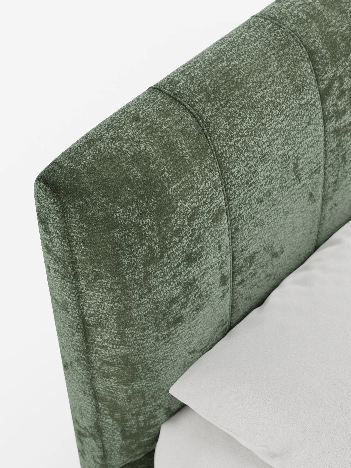 Un primo piano della testiera verticale con trapuntatura a canali, color verde salvia, di un letto imbottito ONYX con vano contenitore, realizzata in tessuto certificato Oeko-Tex®, che mette in risalto il tessuto testurizzato dietro un cuscino grigio chiaro su sfondo bianco.