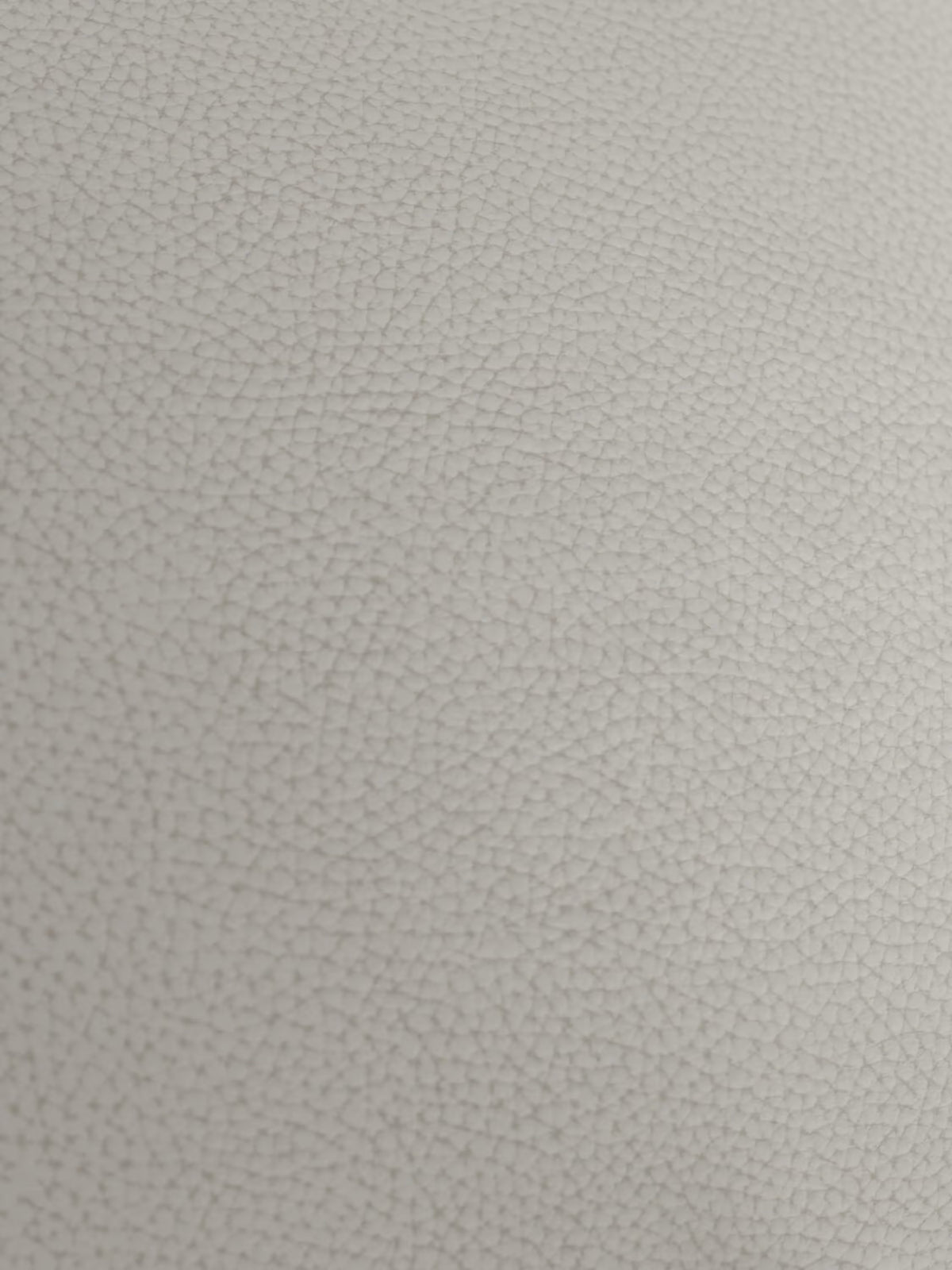 Primo piano della superficie strutturata, di colore grigio chiaro o bianco sporco, del divano Chester 4 Posti 3 sedute in Vera Pelle – Chesterfield Capitonné Artigianale di Divani.Store, che mette in risalto la raffinata trama a granelli, caratteristica della vera pelle italiana. L'illuminazione soffusa accentua la grana uniforme e le delicate variazioni di colore, evocando la maestria artigianale e la prestigiosa qualità del Made in Italy per cui Divani.Store è rinomato.