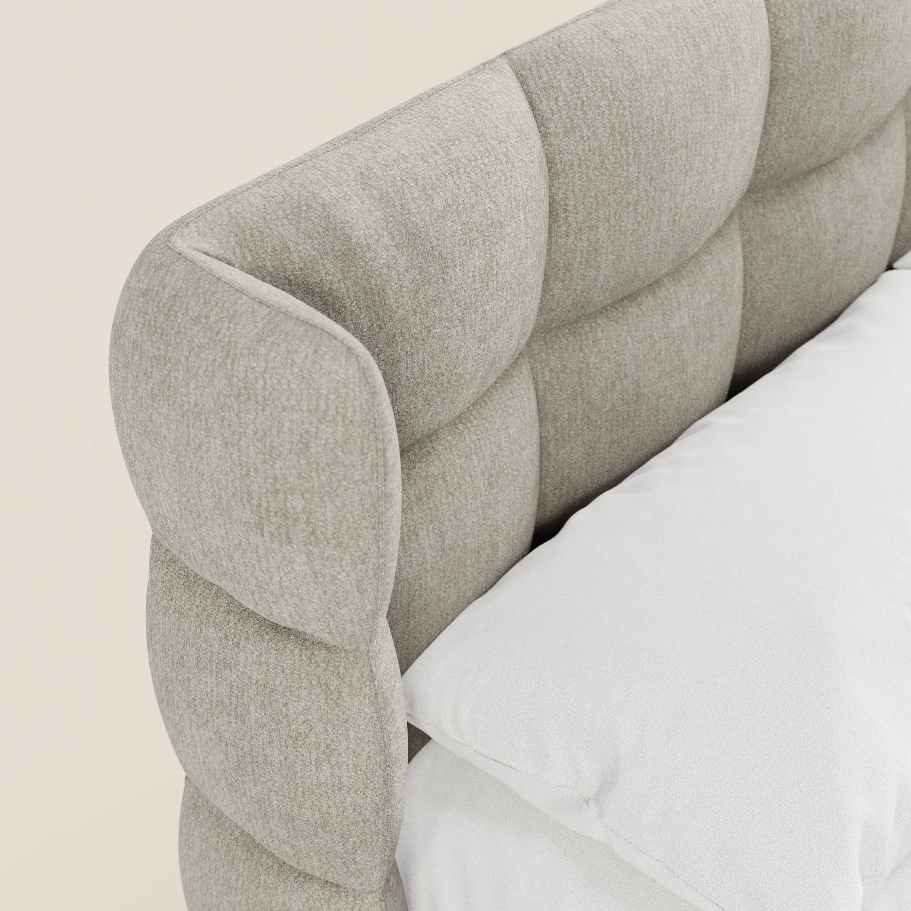 Primo piano del modello RAGNAR di Letti.store: un elegante letto imbottito beige certificato Oeko-Tex®, con una morbida testiera capitonné dal motivo a griglia e cuciture profonde. Un cuscino bianco è appoggiato alla testiera imbottita; lo sfondo è di un colore chiaro e neutro.