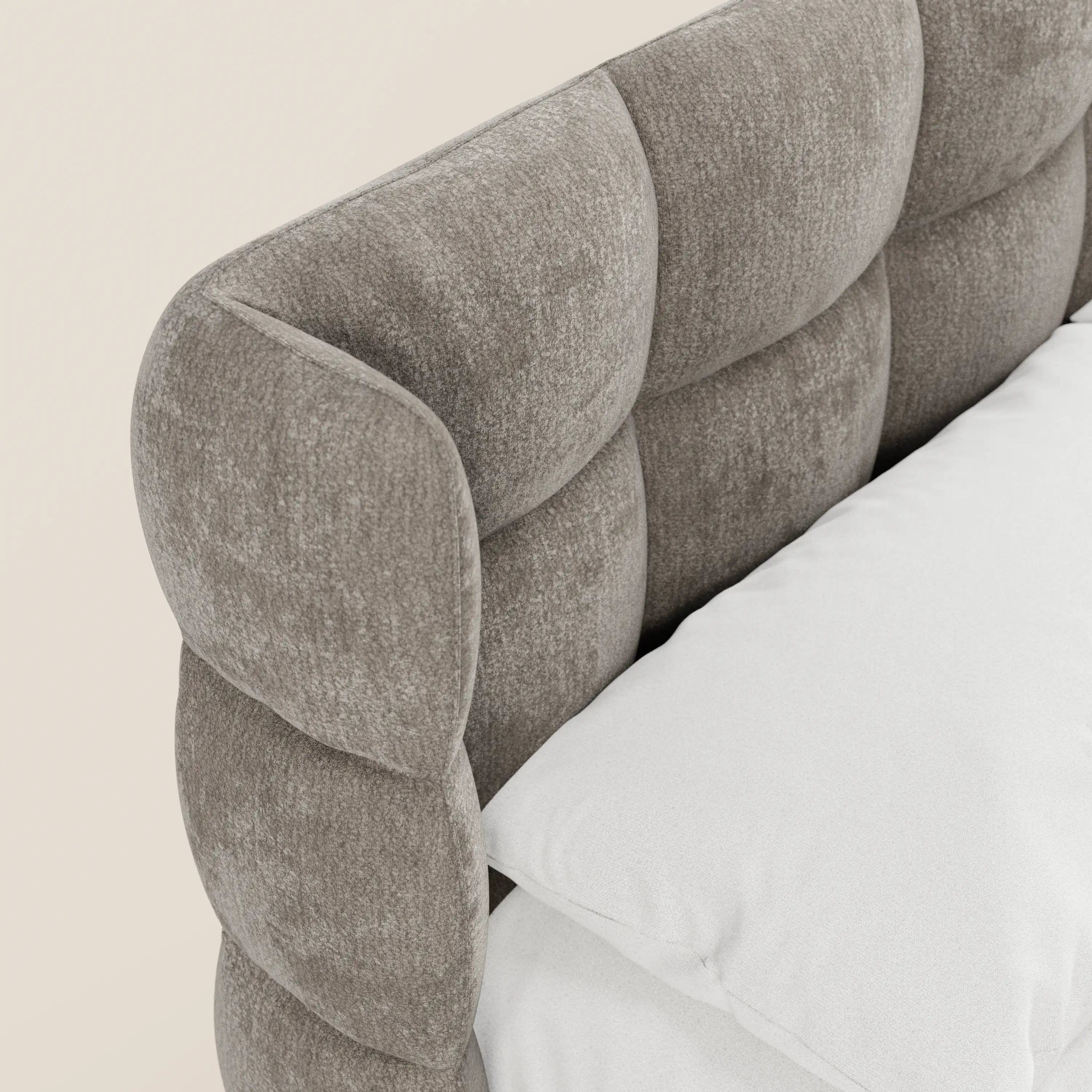Primo piano del letto imbottito RAGNAR con contenitore e testiera capitonné avvolgente in elegante tessuto certificato Oeko-Tex® di Letti.store, caratterizzato da una morbida testiera grigia e da un cuscino bianco che creano un look moderno e accogliente su uno sfondo beige.