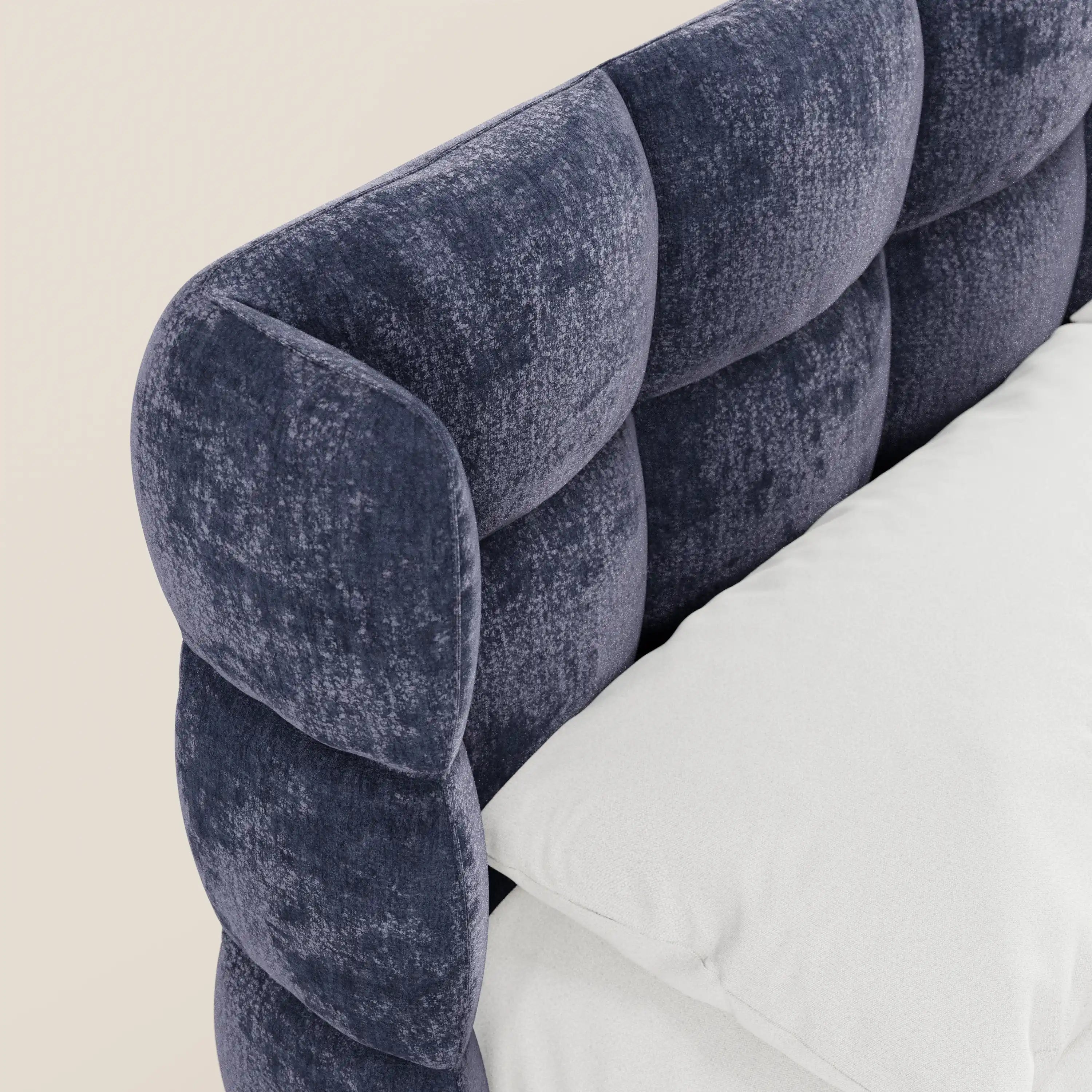 Un primo piano del letto imbottito con contenitore RAGNAR di Letti.store mette in risalto una testiera avvolgente capitonné in elegante tessuto Oeko-Tex®, abbinata a morbida biancheria da letto bianca, il tutto su uno sfondo beige a tinta unita.