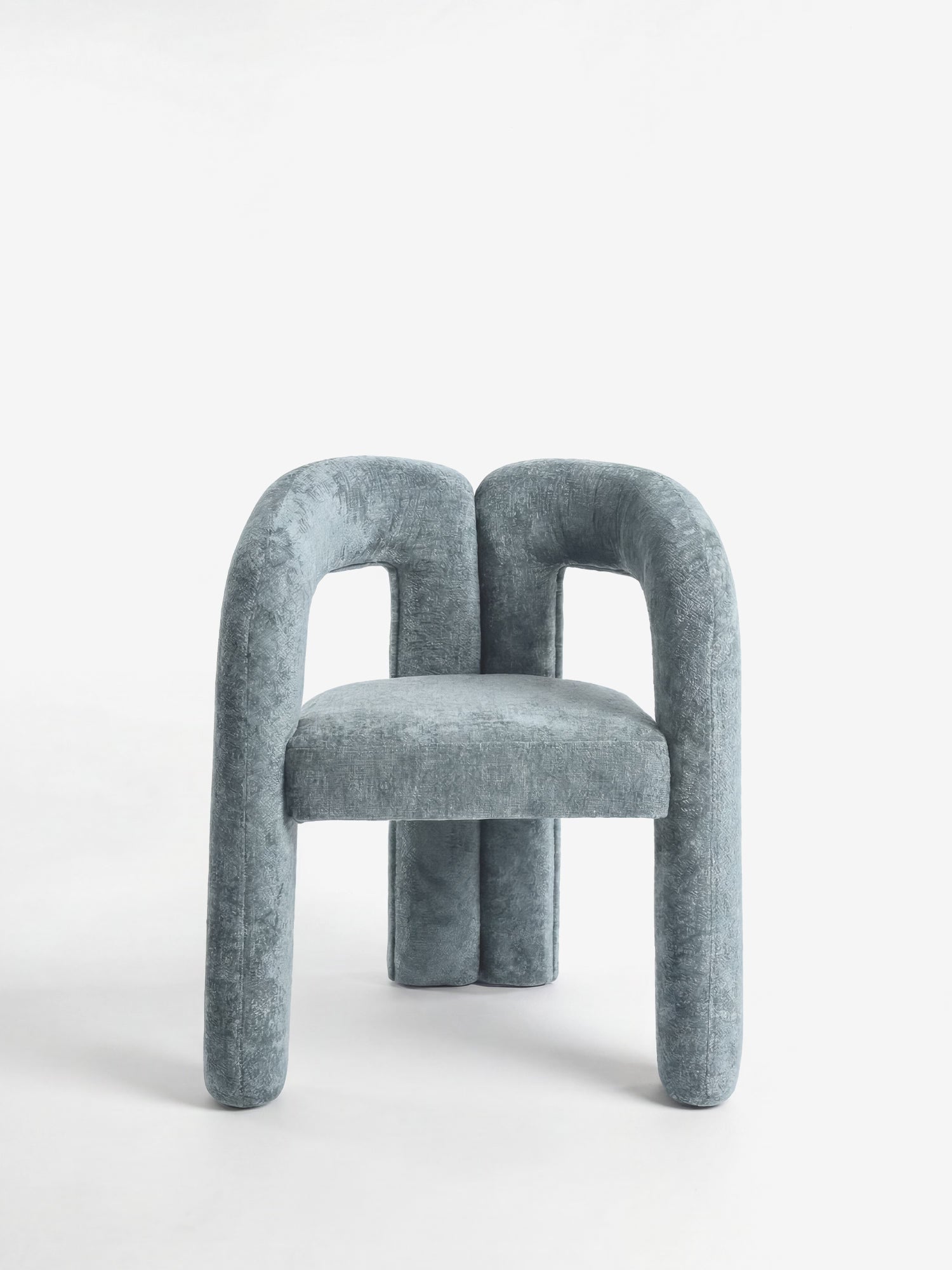 La sedia di design Sibilla di Divani.Store presenta un morbido rivestimento blu, gambe cilindriche e spesse e una forma sinuosa. La sua struttura, interamente rivestita in tessuto, è raffigurata su uno sfondo bianco a tinta unita, che ne esalta lo stile scultoreo e contemporaneo.