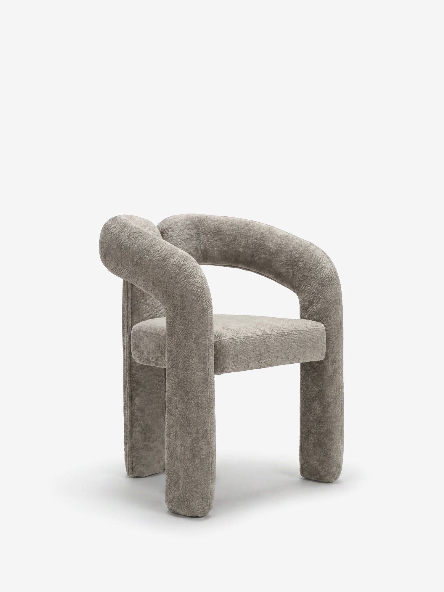 La sedia di design imbottita Sibilla di Divani.Store presenta un morbido rivestimento grigio chiaro, una trama simile al velluto e gambe e braccioli spessi e arrotondati che formano una curva continua. La sua forma minimalista ad arco risalta su uno sfondo bianco liscio.
