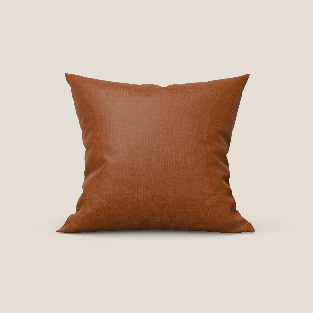 Il cuscino Aspen in elegante tessuto morbido smacchiabile T17 arancio di Divani.Store, di forma quadrata e di colore arancione bruciato, è posizionato in verticale su uno sfondo color crema, con il suo tessuto felpato che cattura la luce naturale da destra.