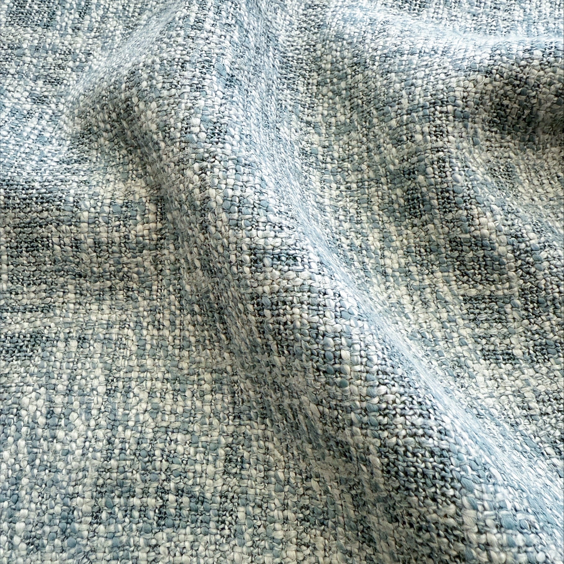 Primo piano di T34 Earthwild di Divani.Store, un sofisticato tessuto a fantasia naturale e pratica nei colori blu chiaro e bianco. La sua superficie morbida e strutturata a intreccio di canestri è smacchiabile e ha un aspetto accogliente e tattile.