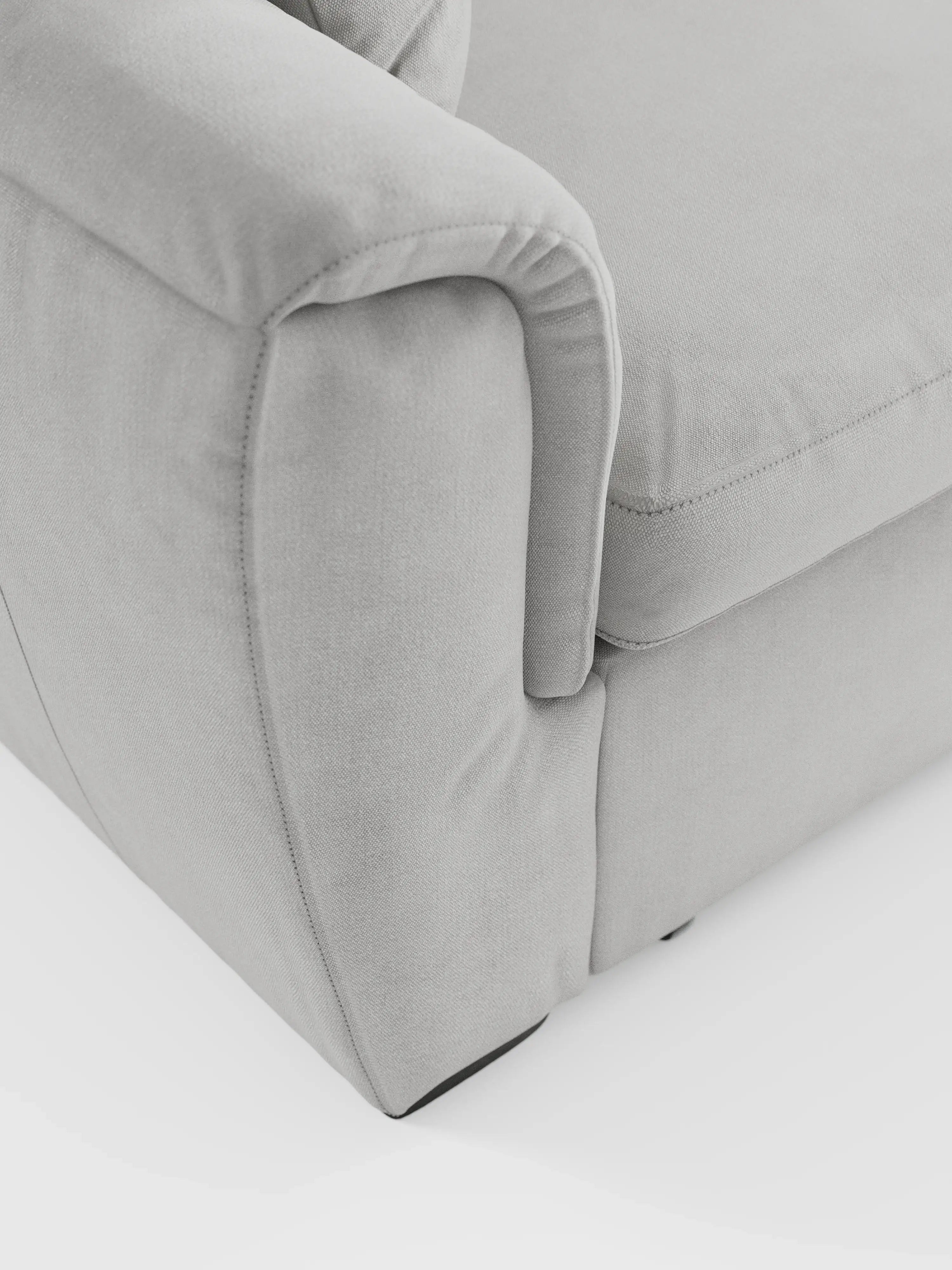 Primo piano di un divano Titano a 2 posti estraibile, color grigio chiaro, con poggiatesta reclinabili in tessuto smacchiabile Oeko-Tex®, di Divani.Store, che mette in risalto la morbida trama del tessuto, le cuciture delicate e i bordi arrotondati dei cuscini dei braccioli e della seduta. Questo divano moderno e compatto appare lussuoso con ombre minime su uno sfondo bianco, mostrando solo una parte del bracciolo e della base.