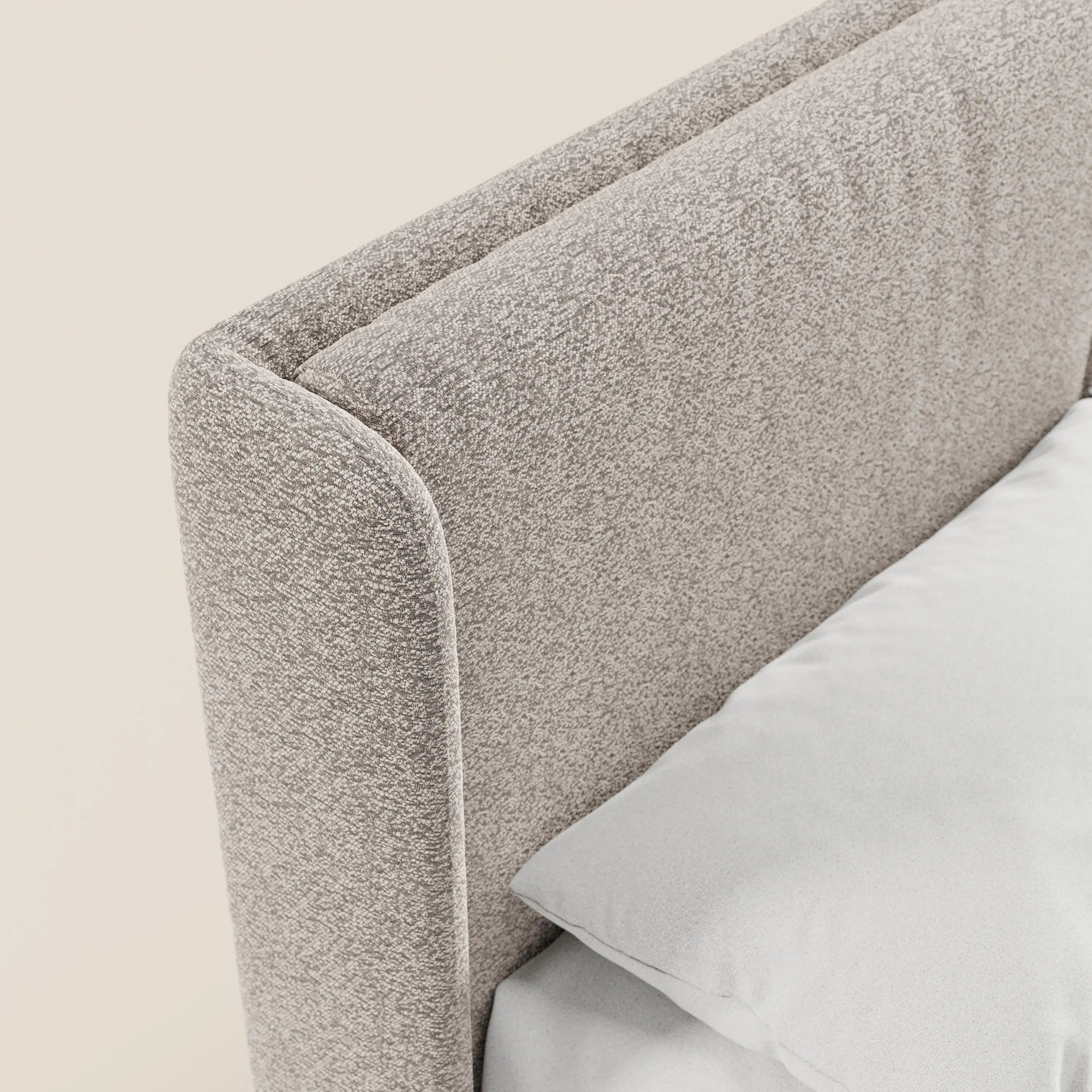 Primo piano del letto di design VALKIRIA di Letti.store, caratterizzato da una testiera in tessuto grigio chiaro certificato Oeko-Tex®, con 2 morbidi cuscini e una base contenitiva. La biancheria da letto bianca ne esalta lo stile contemporaneo sullo sfondo chiaro.