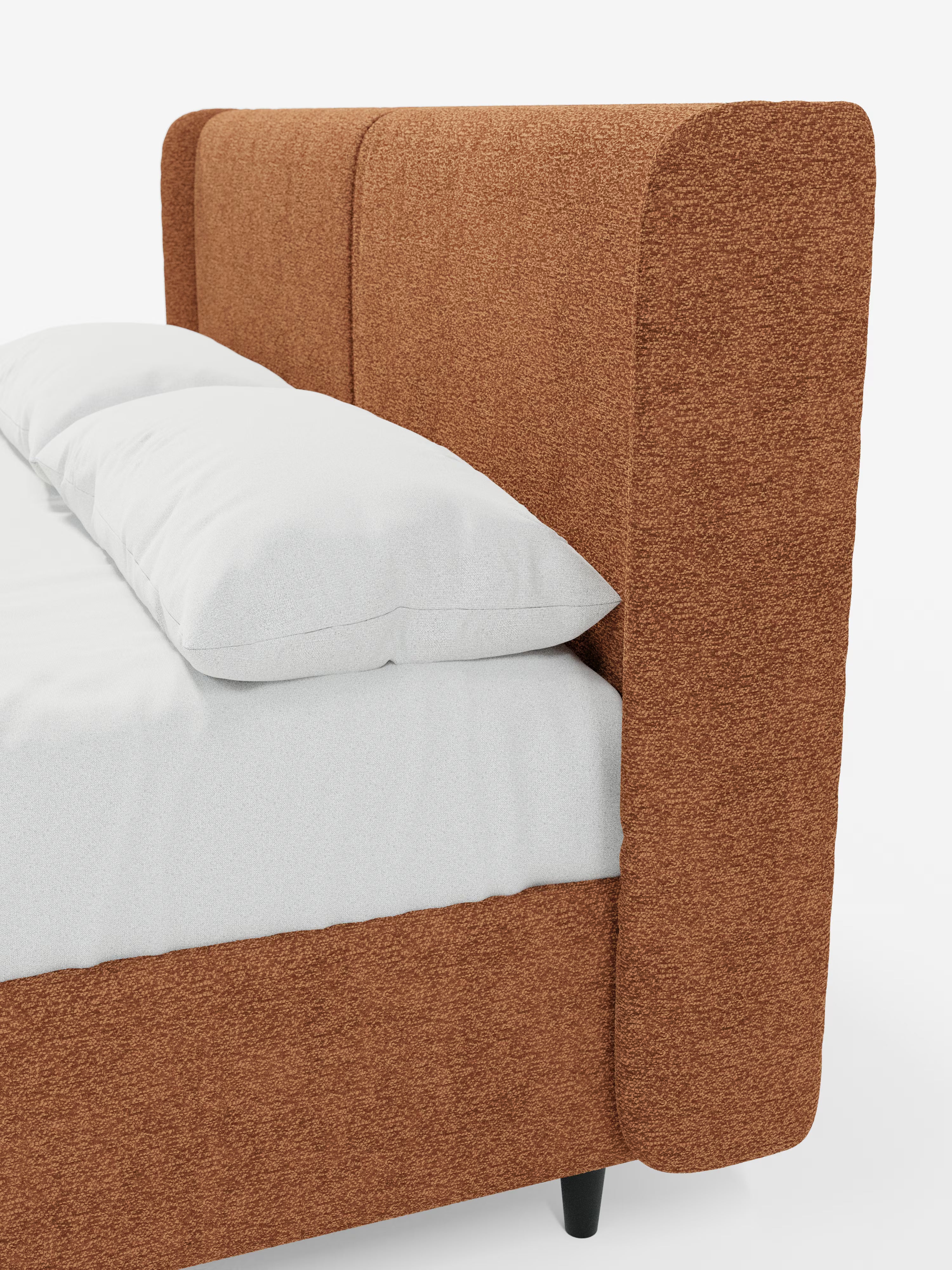 Primo piano del letto di design VALKIRIA con contenitore e testiera avvolgente di Letti.store, che mette in risalto la sua testiera alta, imbottita, color ruggine e dai bordi arrotondati. Il letto è abbinato a un materasso bianco e a due cuscini bianchi, e presenta gambe corte di colore nero. La sua estetica contemporanea risalta sullo sfondo bianco a tinta unita.