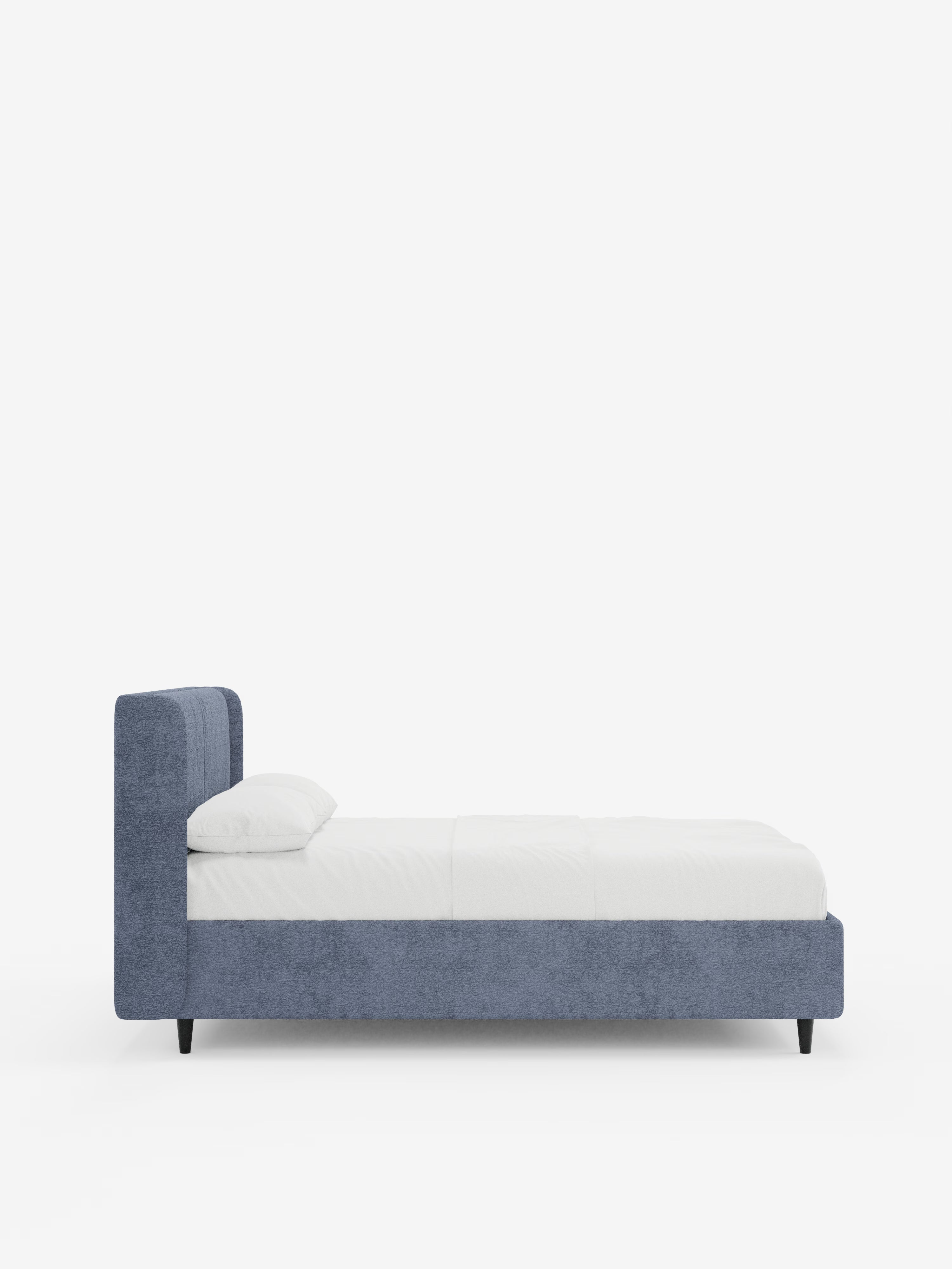 Una vista laterale del letto di design VALKIRIA con vano contenitore e testiera avvolgente di Letti.store, caratterizzato da una struttura rivestita in tessuto azzurro certificato Oeko-Tex® con gambe corte nere, un materasso bianco e due cuscini imbottiti, il tutto su uno sfondo bianco a tinta unita per esaltarne il design elegante e contemporaneo.
