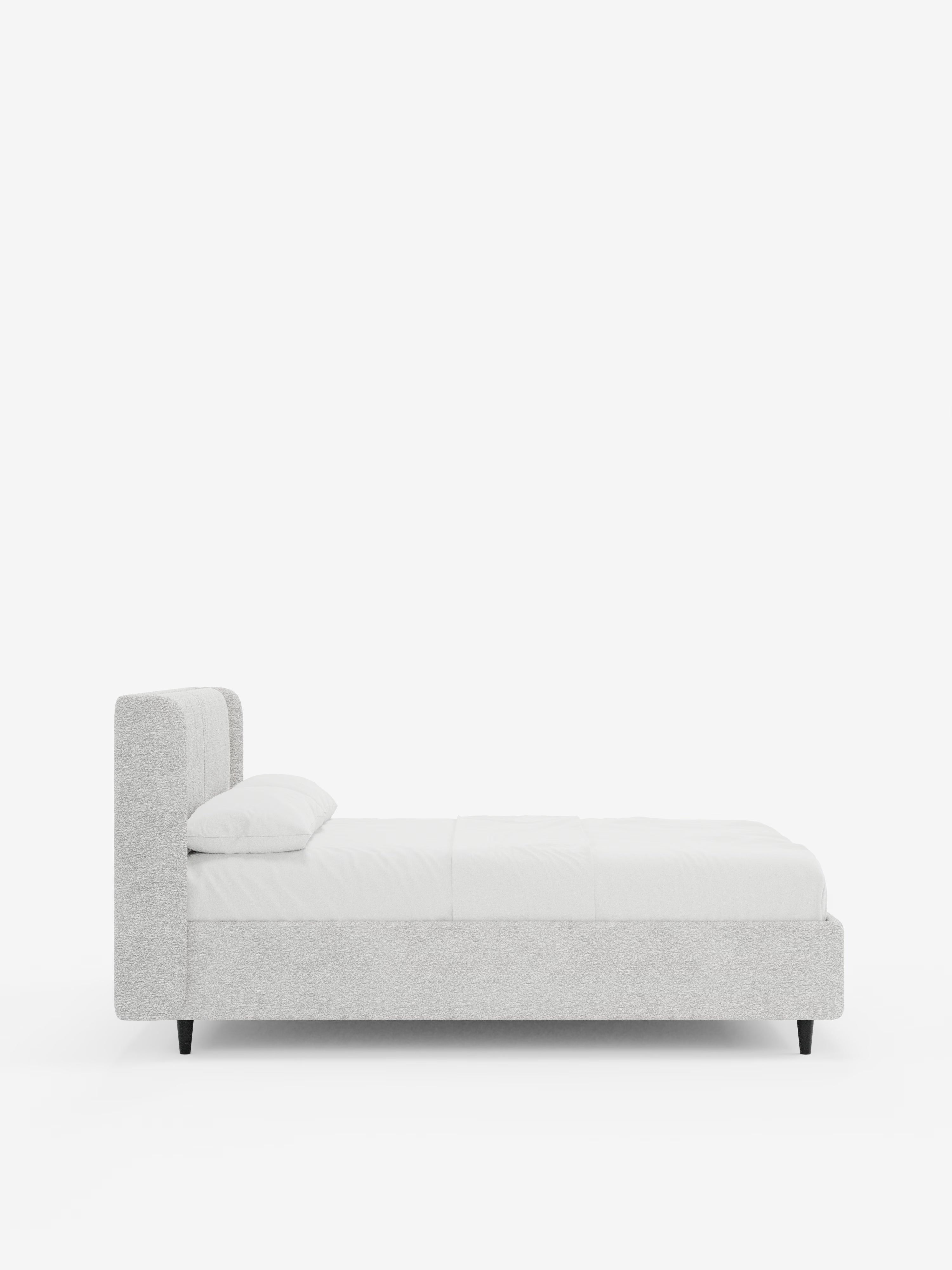 Il letto di design VALKIRIA con contenitore e testiera avvolgente di Letti.store è qui raffigurato di profilo, in una moderna versione rivestita in grigio chiaro. Questo letto contemporaneo presenta gambe nere e una testiera bassa e avvolgente, impreziosita da due cuscini imbottiti in tessuto Oeko-Tex®. Il letto è elegantemente rivestito con biancheria da letto bianca e un unico cuscino, su uno sfondo bianco a tinta unita.