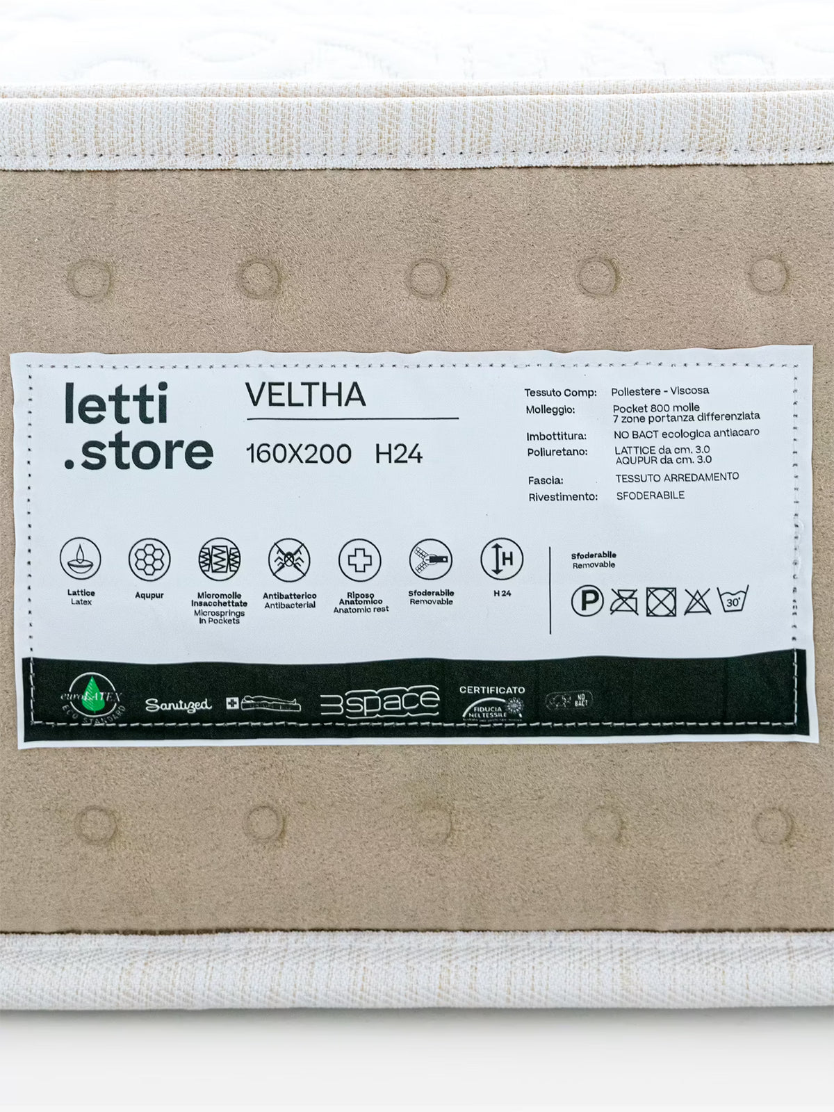 Un primo piano dell’etichetta di un materasso di Divani.Store, modello VELTHA – Materasso Bio-Adattivo con molle insacchettate e Lattice Naturale a 7 zone, misura 160x200 cm con un’altezza di 24 cm. L'etichetta riporta informazioni sui materiali, quali il lattice naturale e le 800 micro-molle insacchettate, oltre ai simboli di lavaggio, alle certificazioni e ai pittogrammi che evidenziano caratteristiche quali traspirabilità, supporto ortopedico e materasso a 7 zone differenziate.