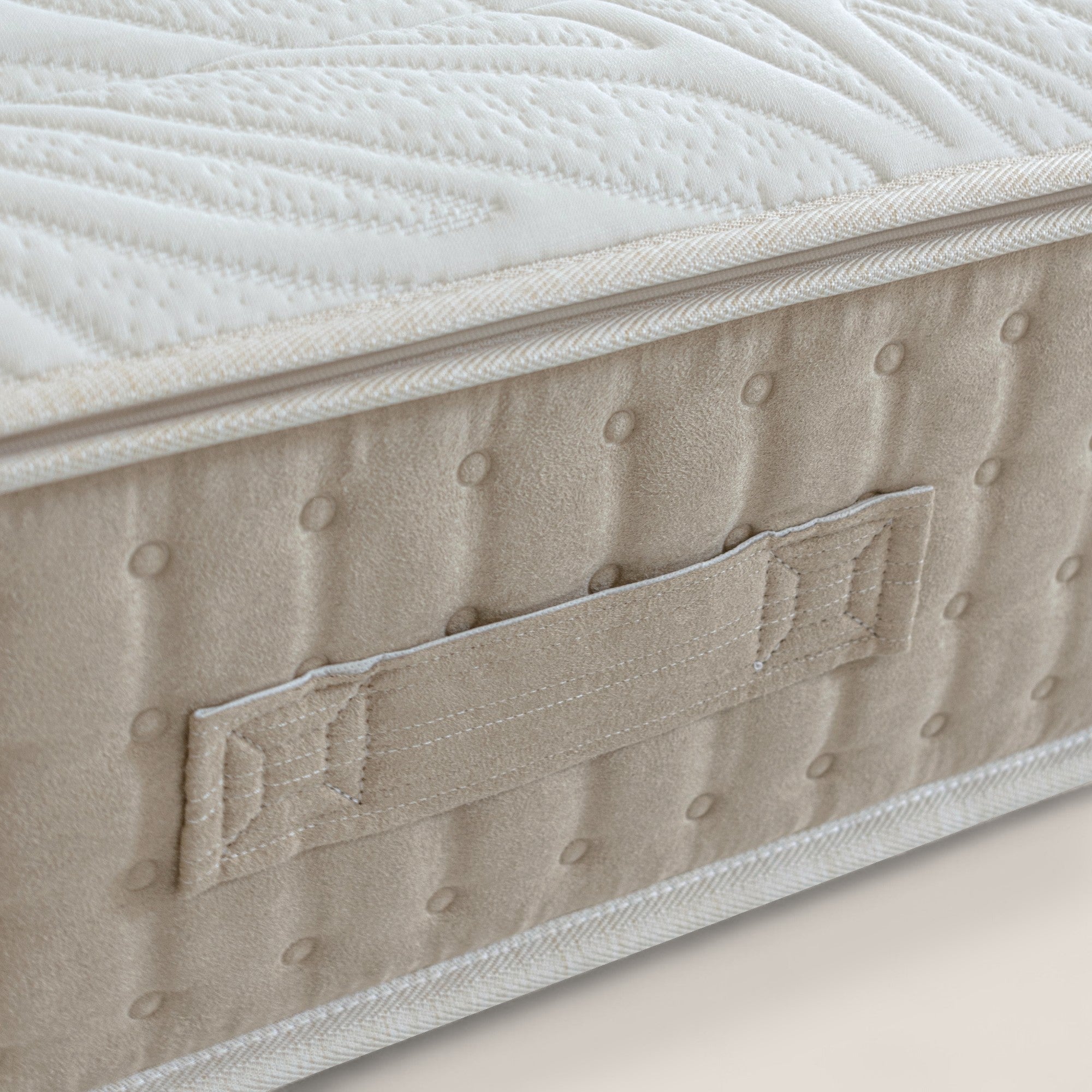 Primo piano di VELTHA di Divani.Store: lato beige con maniglia in tessuto impunturato, reticolo in lattice naturale e texture trapuntata. Il top bianco presenta un motivo a onde e un bordino che riflette la qualità artigianale e il supporto differenziato a 7 zone.