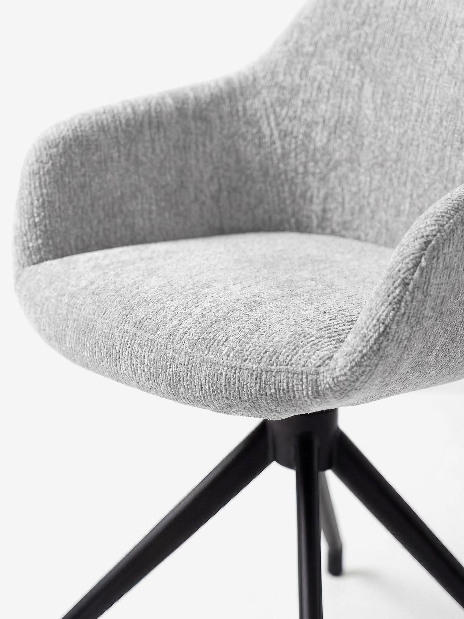 Un primo piano della sedia imbottita Vico di Divani.Store, caratterizzata da un tessuto grigio chiaro morbido al tatto certificato OEKO-TEX®, braccioli ricurvi e una base a quattro gambe in metallo nero, ne mette in risalto il design contemporaneo su uno sfondo bianco a tinta unita.