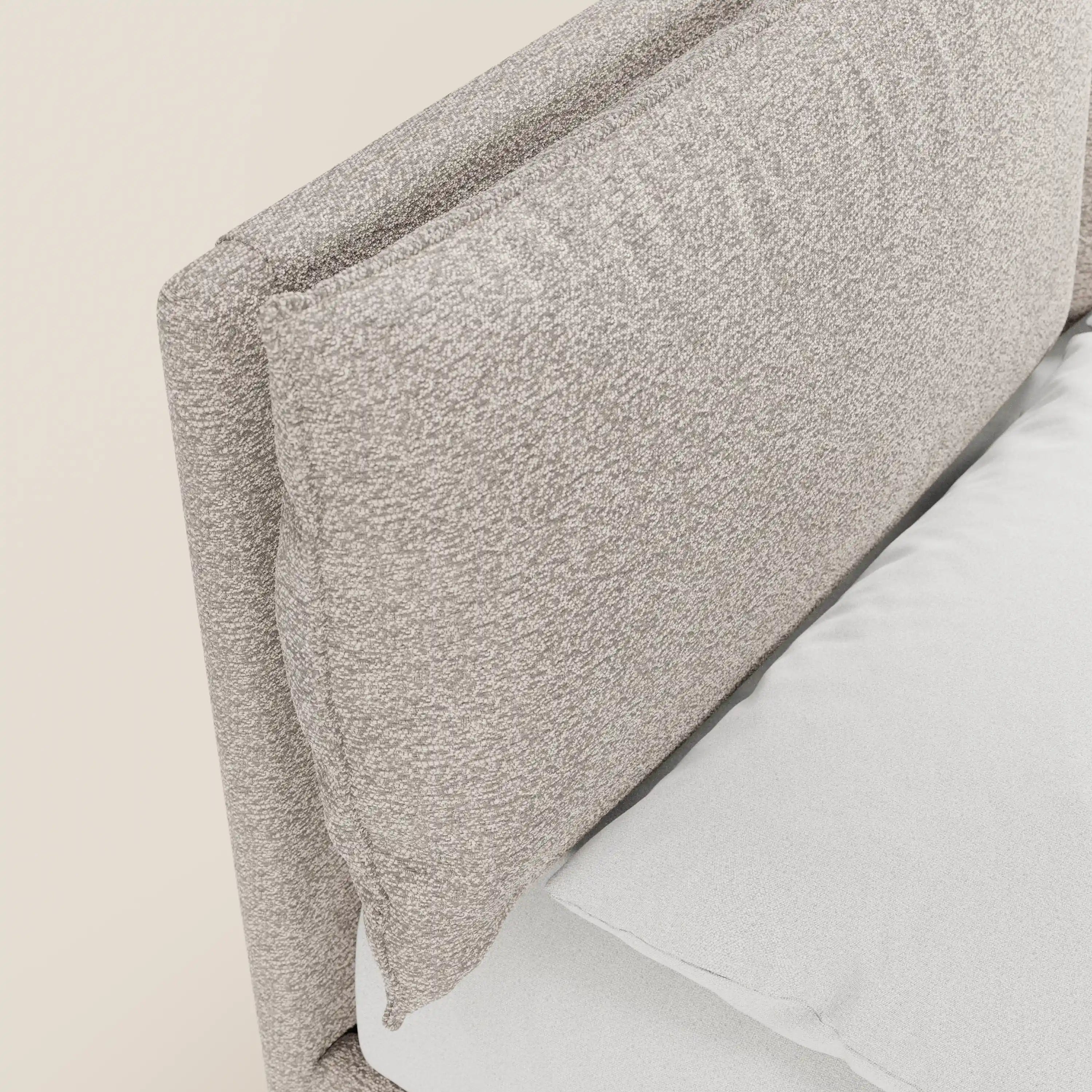 Primo piano del letto imbottito ZAYRON di Letti.store: una testiera imbottita color beige chiaro, certificata Oeko-Tex®, con morbidi cuscini regolabili. Il cuscino bianco e il materasso esaltano l’eleganza moderna e lo spazio di contenimento nascosto di questo letto di grande stile.