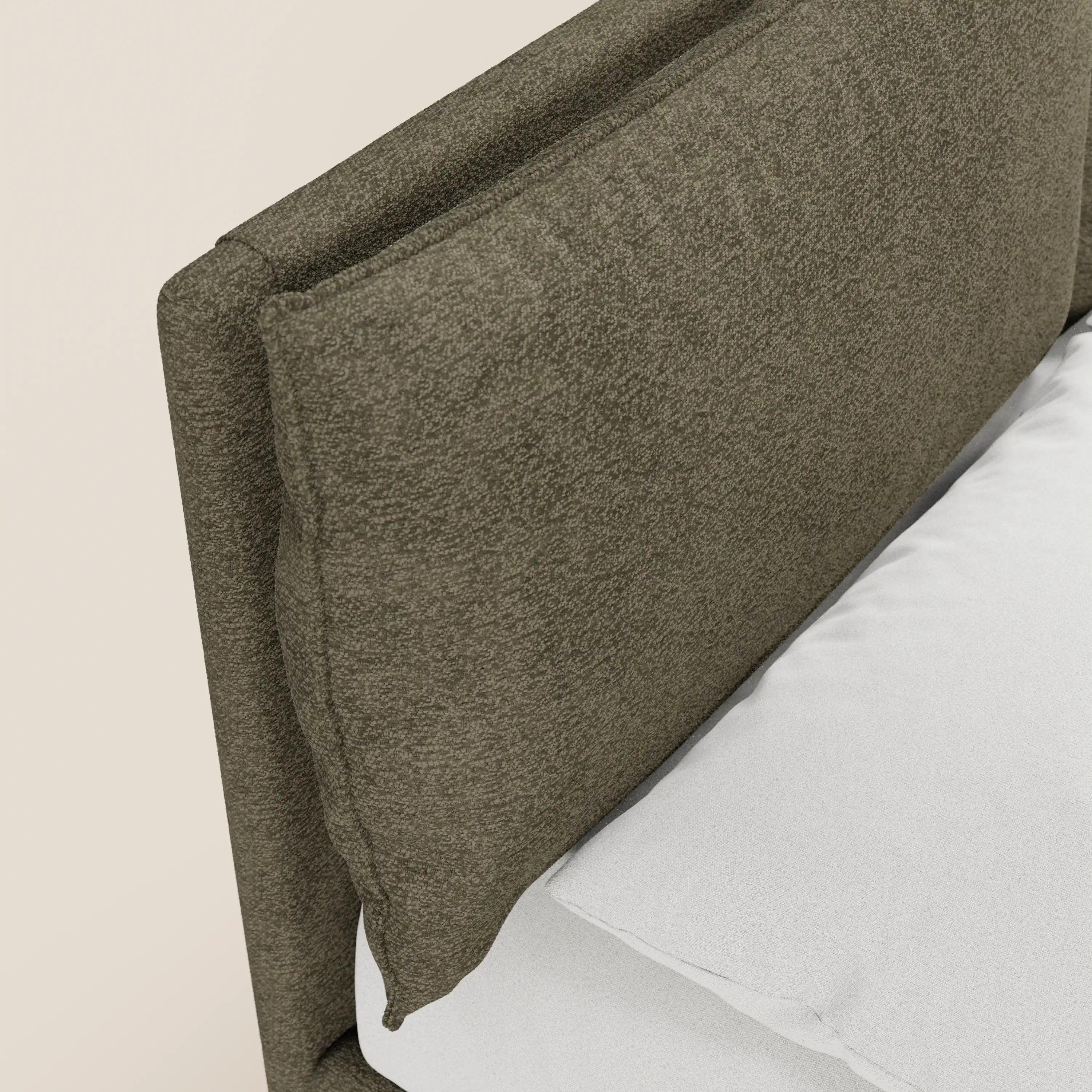 Primo piano del letto imbottito con contenitore ZAYRON di Letti.store, caratterizzato da una testiera in tessuto verde oliva certificato Oeko-Tex® con morbidi cuscini regolabili. Il letto è rivestito con biancheria da letto di un bianco brillante su uno sfondo beige chiaro.