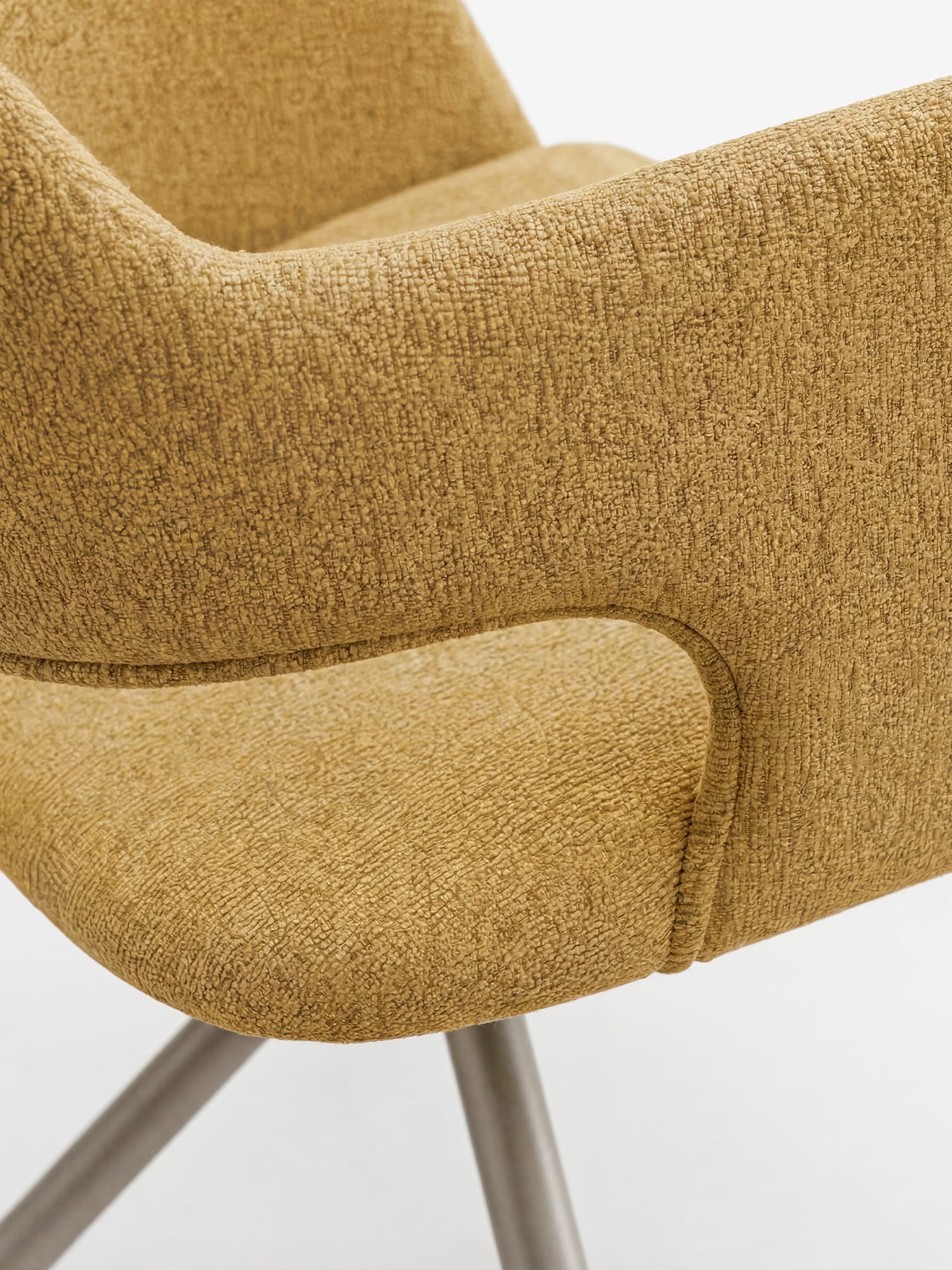 Primo piano della sedia imbottita di design Zefira di Divani.Store, caratterizzata da un rivestimento in tessuto effetto cotone color marrone chiaro, braccioli ricurvi, seduta imbottita ed eleganti gambe angolate in metallo color champagne su uno sfondo bianco a tinta unita.