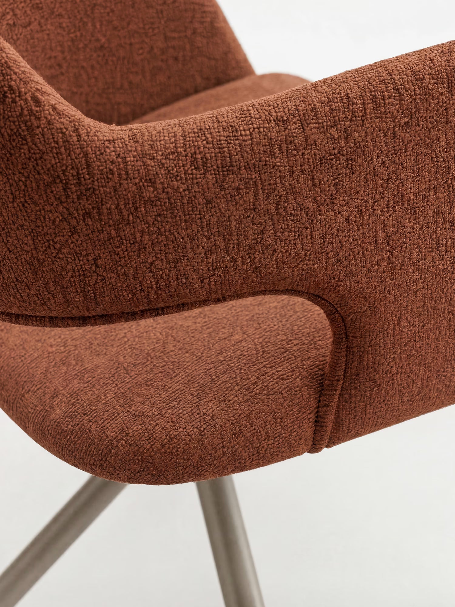 Primo piano della sedia imbottita di design Zefira di Divani.Store, caratterizzata da braccioli ricurvi, tessuto effetto cotone color ruggine e gambe minimaliste in metallo color champagne su uno sfondo bianco a tinta unita.