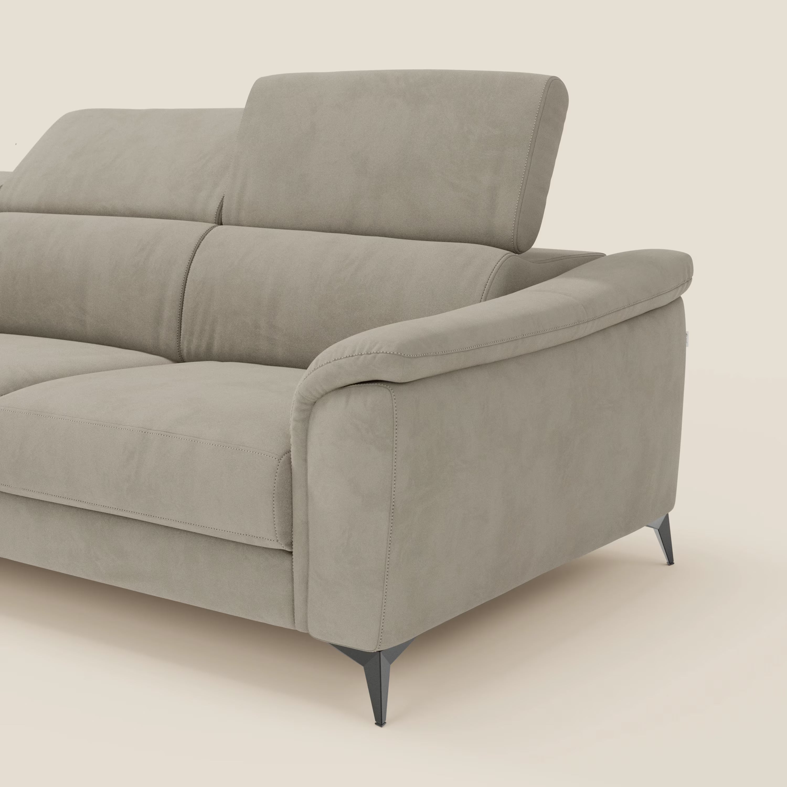 Arcos Divano con penisola di Divani.Store vanta una microfibra impermeabile T11 tortora, gambe alte, braccioli ampi e poggiatesta regolabili. Solo una parte di questo divano moderno con manifattura italiana è visibile su uno sfondo bianco sporco.