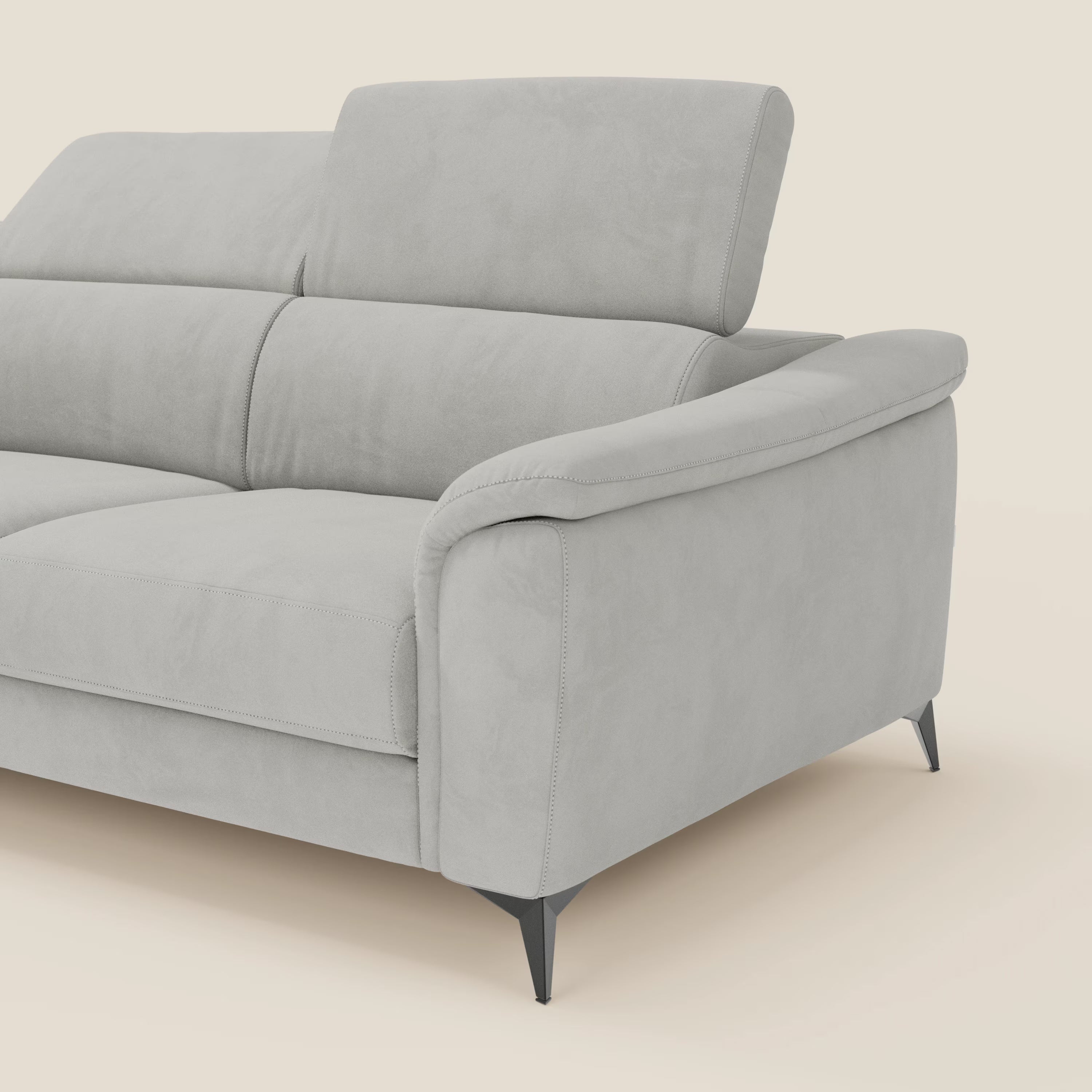 Arcos Divano angolare di Divani.Store è caratterizzato da gambe alte, poggiatesta reclinabili e microfibra grigio chiaro T11 resistente all'acqua. Gli spessi braccioli arrotondati e le eleganti gambe in metallo nero completano il look. Solo una parte del divano appare su un morbido sfondo beige.