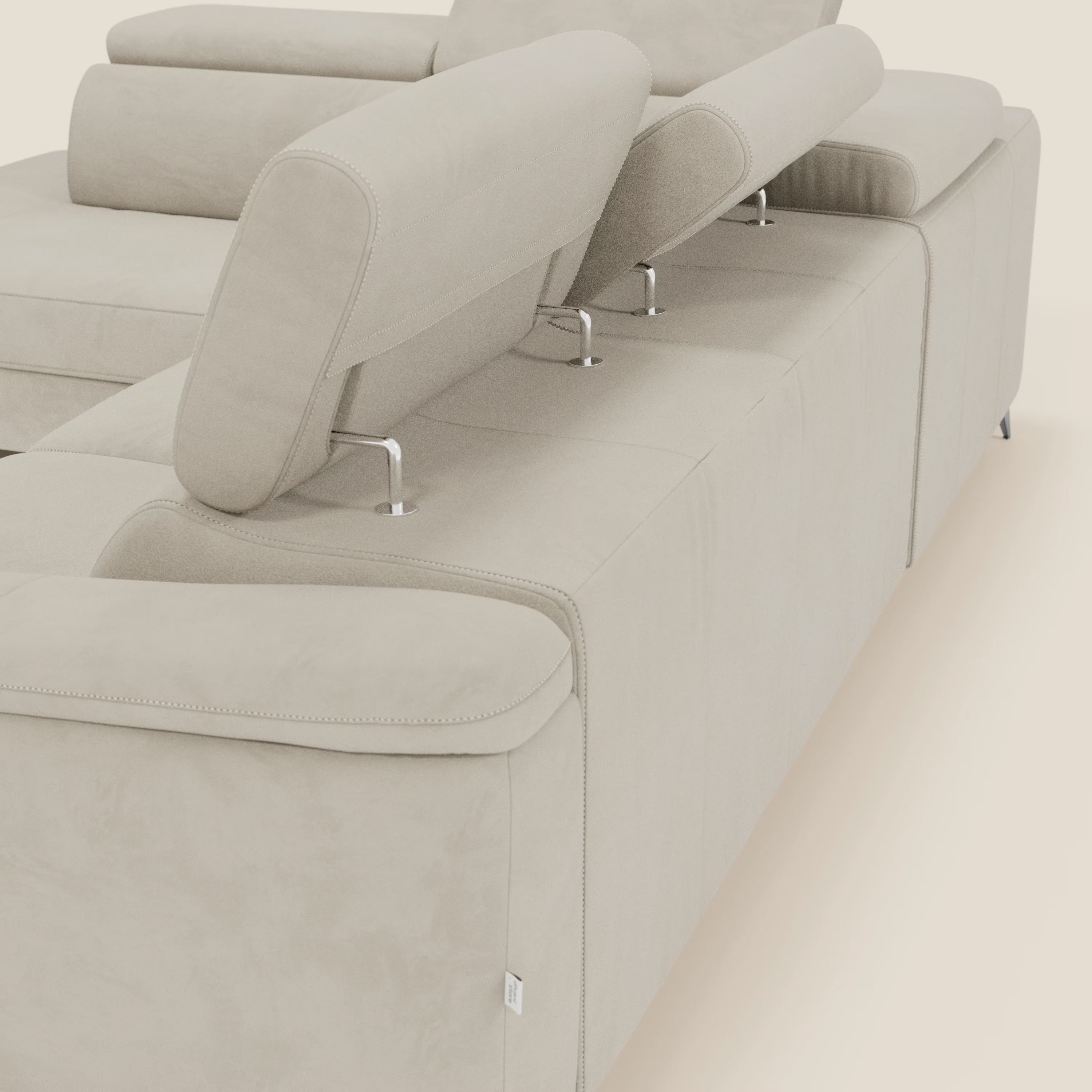 Primo piano angolato di Arcos Divano angolare di Divani.Store, caratterizzato da microfibra impermeabile T11 panna, gambe alte, tre poggiatesta regolabili con supporti cromati, ampi braccioli imbottiti e un'elegante poltrona reclinabile elettrica. Sfondo chiaro in tinta unita.