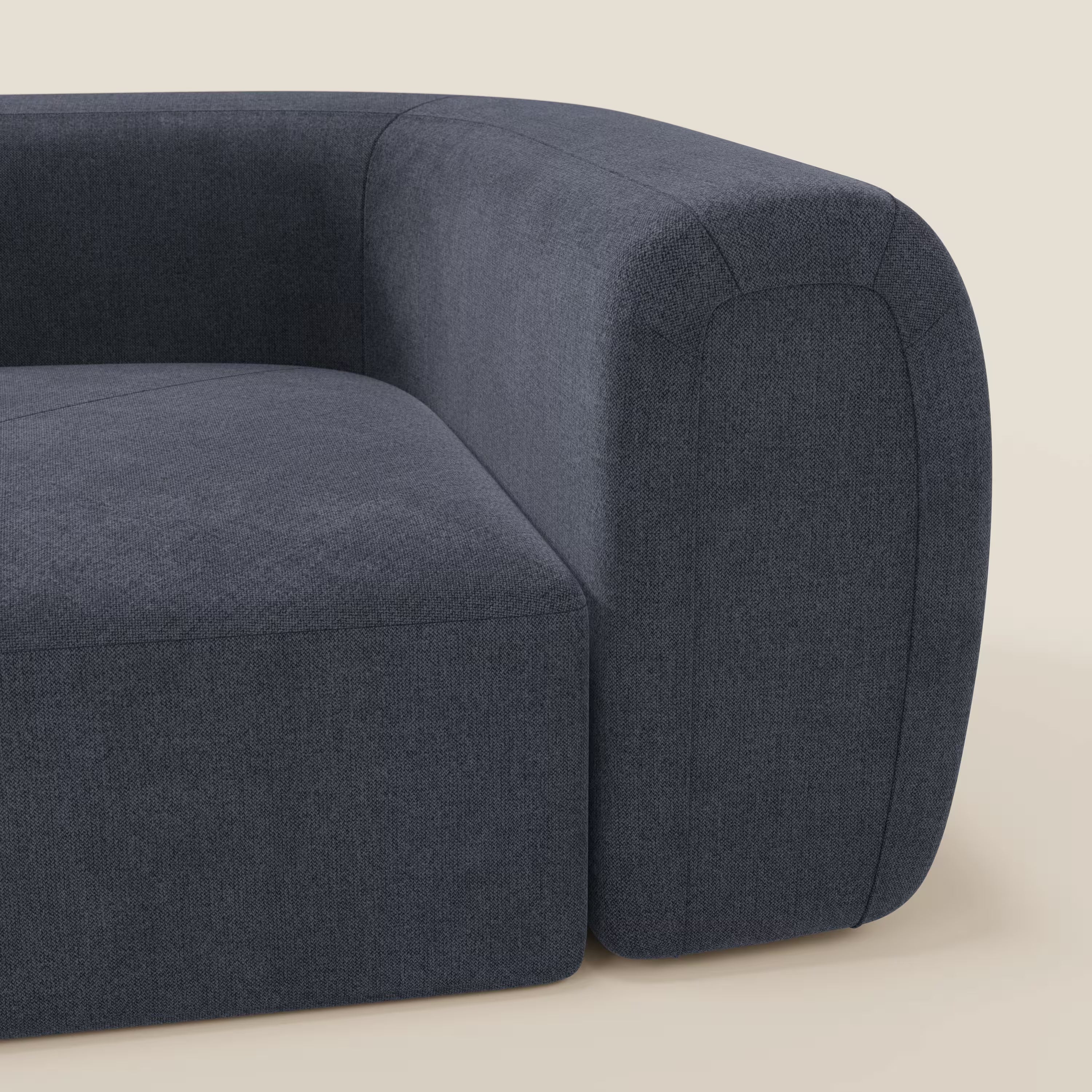 Primo piano di Bonbon Modulo angolare di Divani.Store, un moderno divano componibile in tessuto antimacchia T23 blu ardesia, con braccioli e schienale morbidi e arrotondati, ideale per un arredamento contemporaneo su uno sfondo beige chiaro.