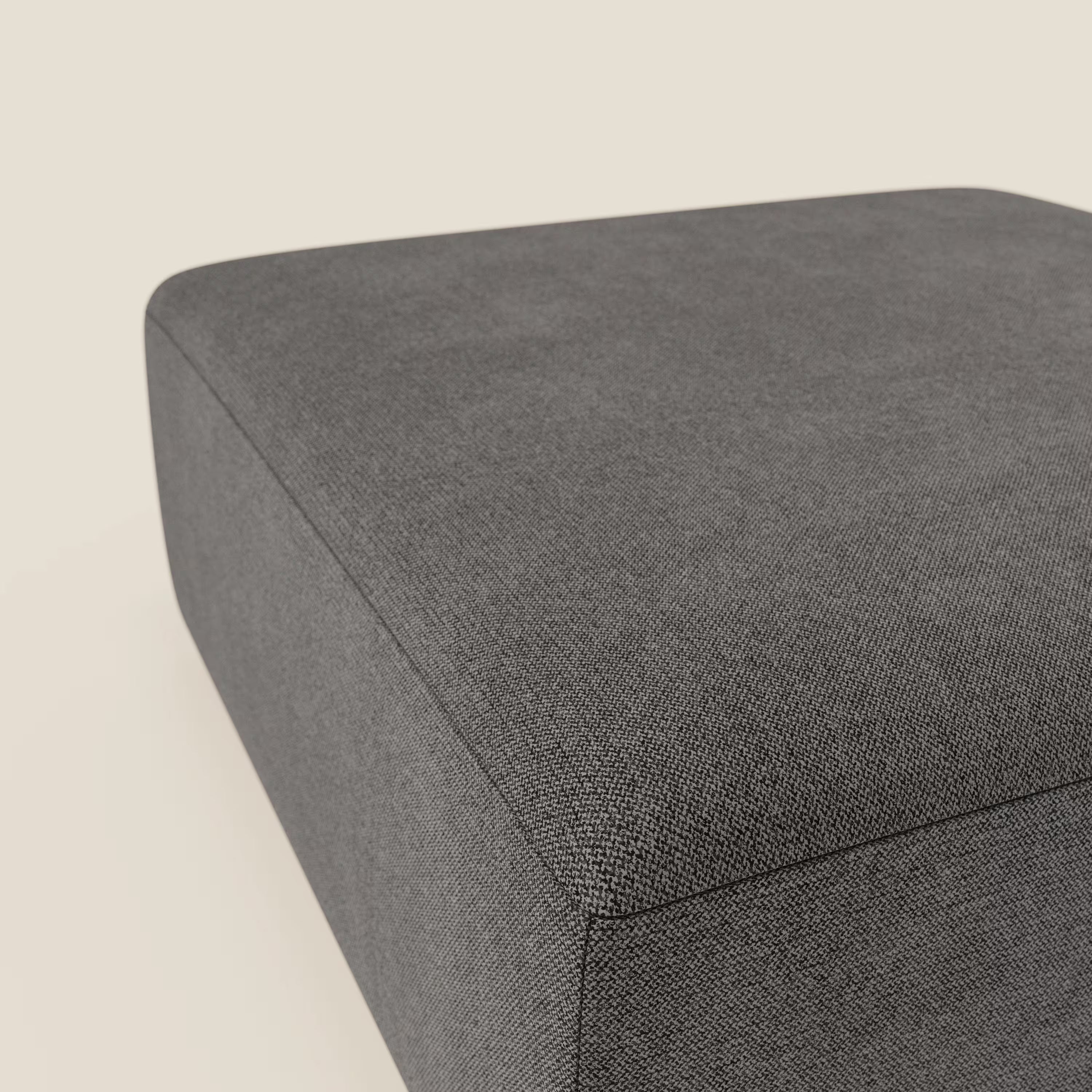 Primo piano del pouf divano modulare BonBon di Divani.Store in tessuto antimacchia T23 antracite, caratterizzato da linee pulite e bordi senza cuciture che ne sottolineano il design minimalista su uno sfondo beige chiaro.