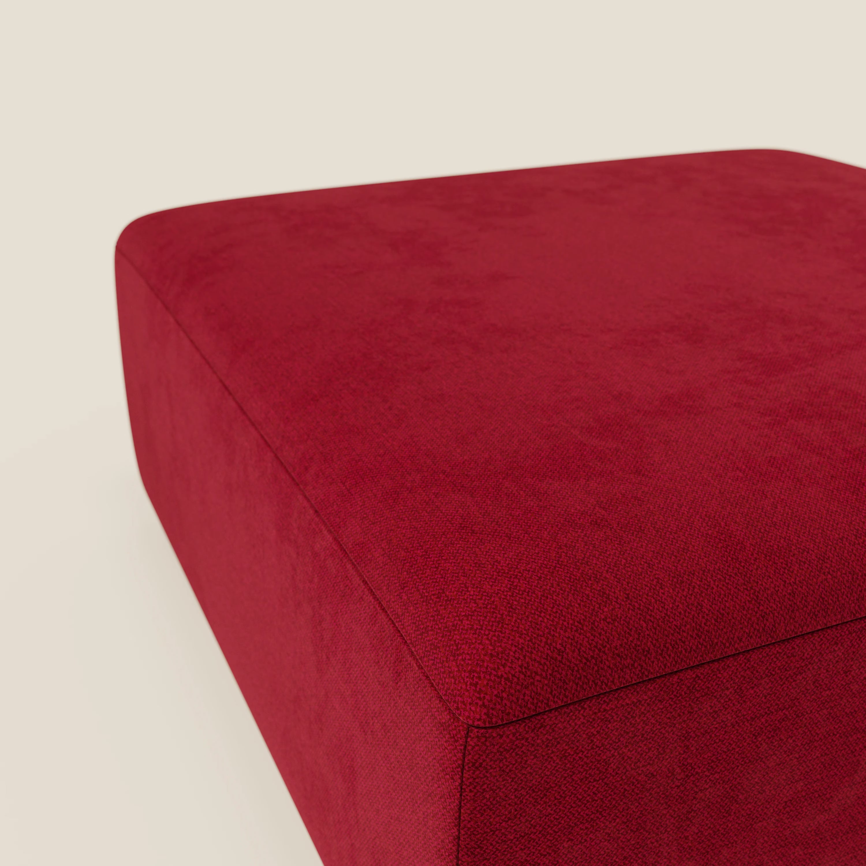 Il pouf divano modulare BonBon di Divani.Store, presentato in tessuto antimacchia T23 bordeaux, è caratterizzato da linee pulite e rivestimento liscio. Il pouf, di forma quadrata e di grandi dimensioni, è posizionato su uno sfondo beige chiaro, che mette in risalto la sua superficie strutturata.