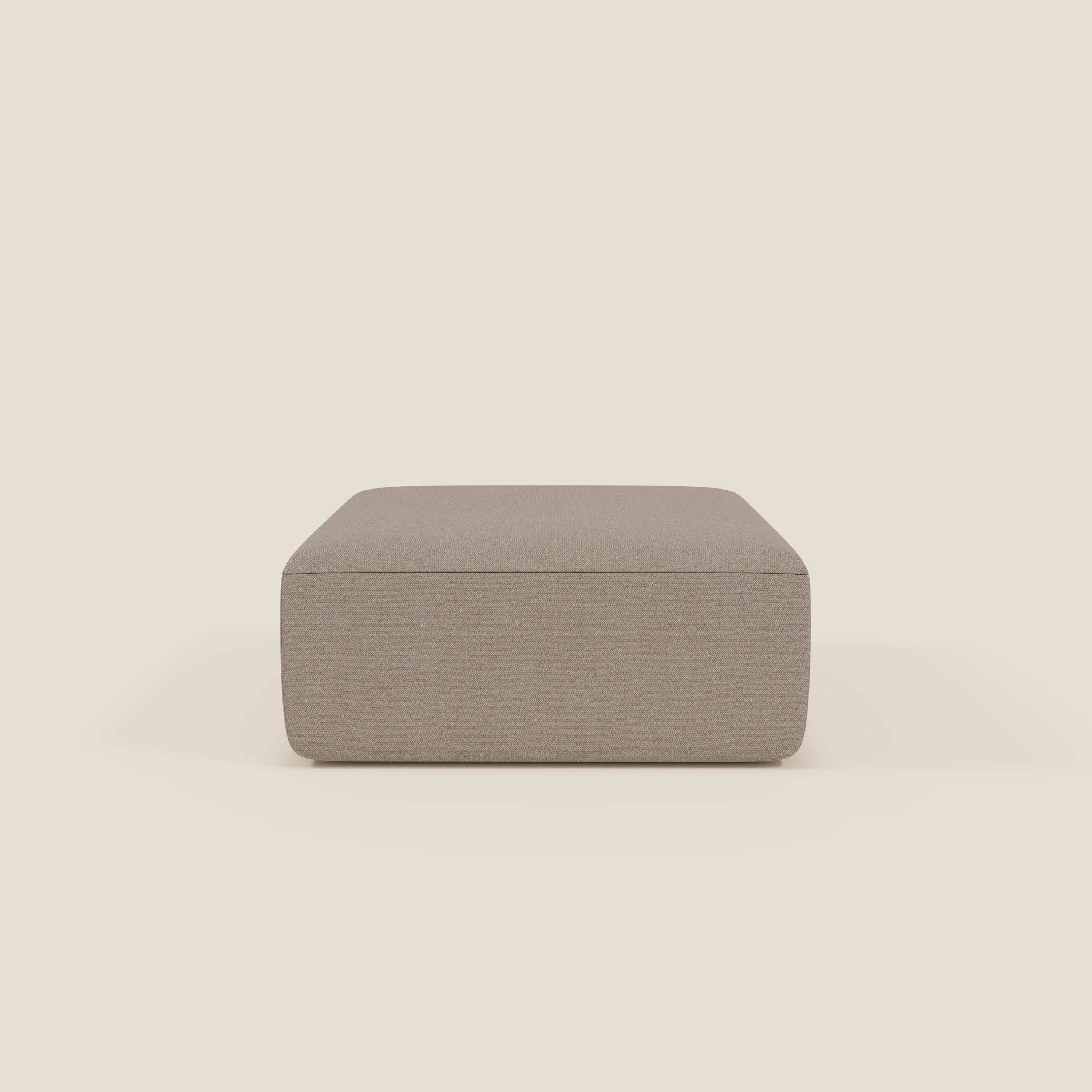 Il pouf divano modulare BonBon di Divani.Store in tessuto smacchiabile T23 tortora è un pouf quadrato e minimalista di colore tortora con un design liscio e senza gambe, presentato al centro su uno sfondo beige chiaro. Disponibile in due misure.