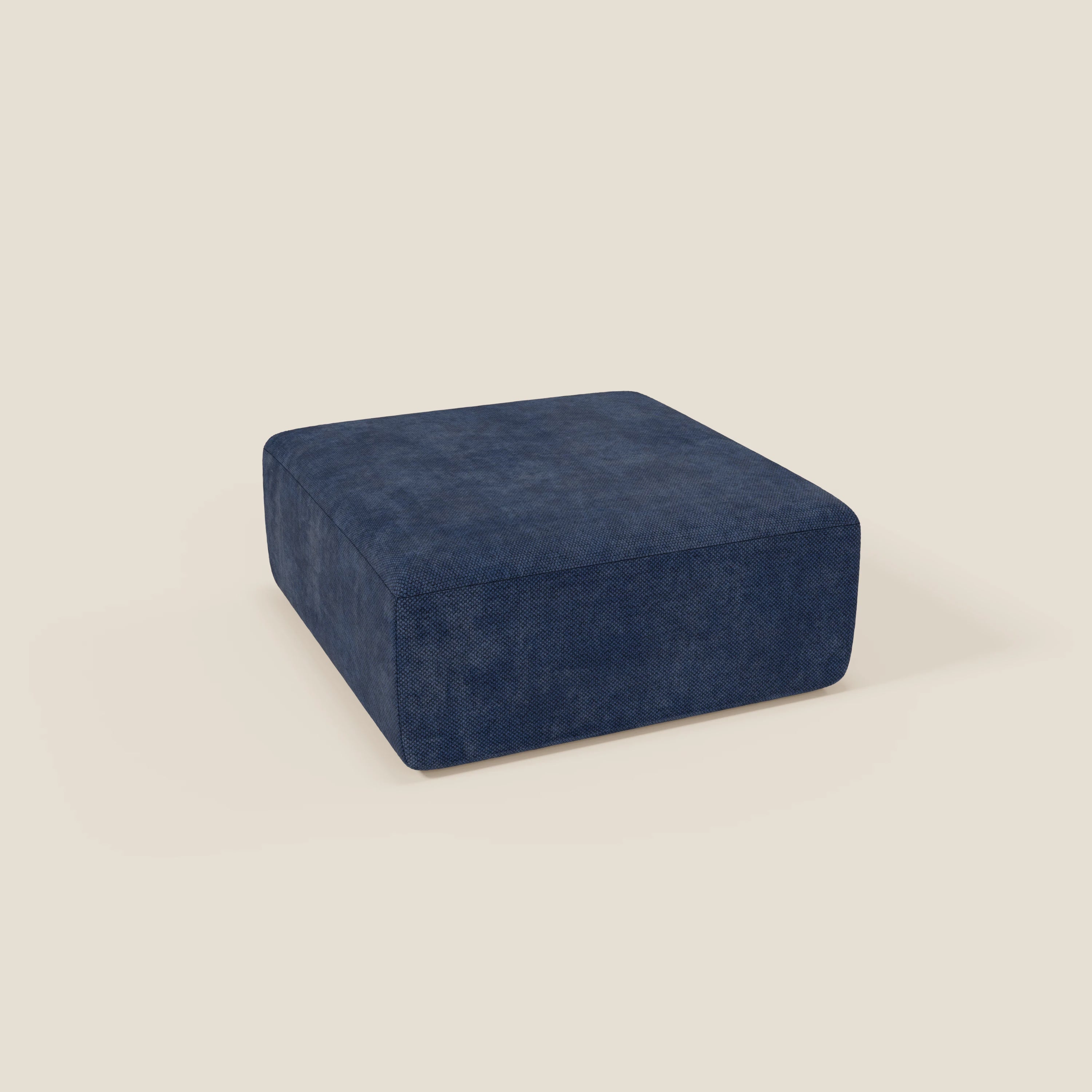 Il pouf BonBon modulo Grande Fratello edition di Divani.Store è un grande pouf quadrato di colore blu navy, con un tessuto morbido e strutturato e un design basso e senza gambe per un look moderno e minimalista, esposto su uno sfondo beige chiaro.